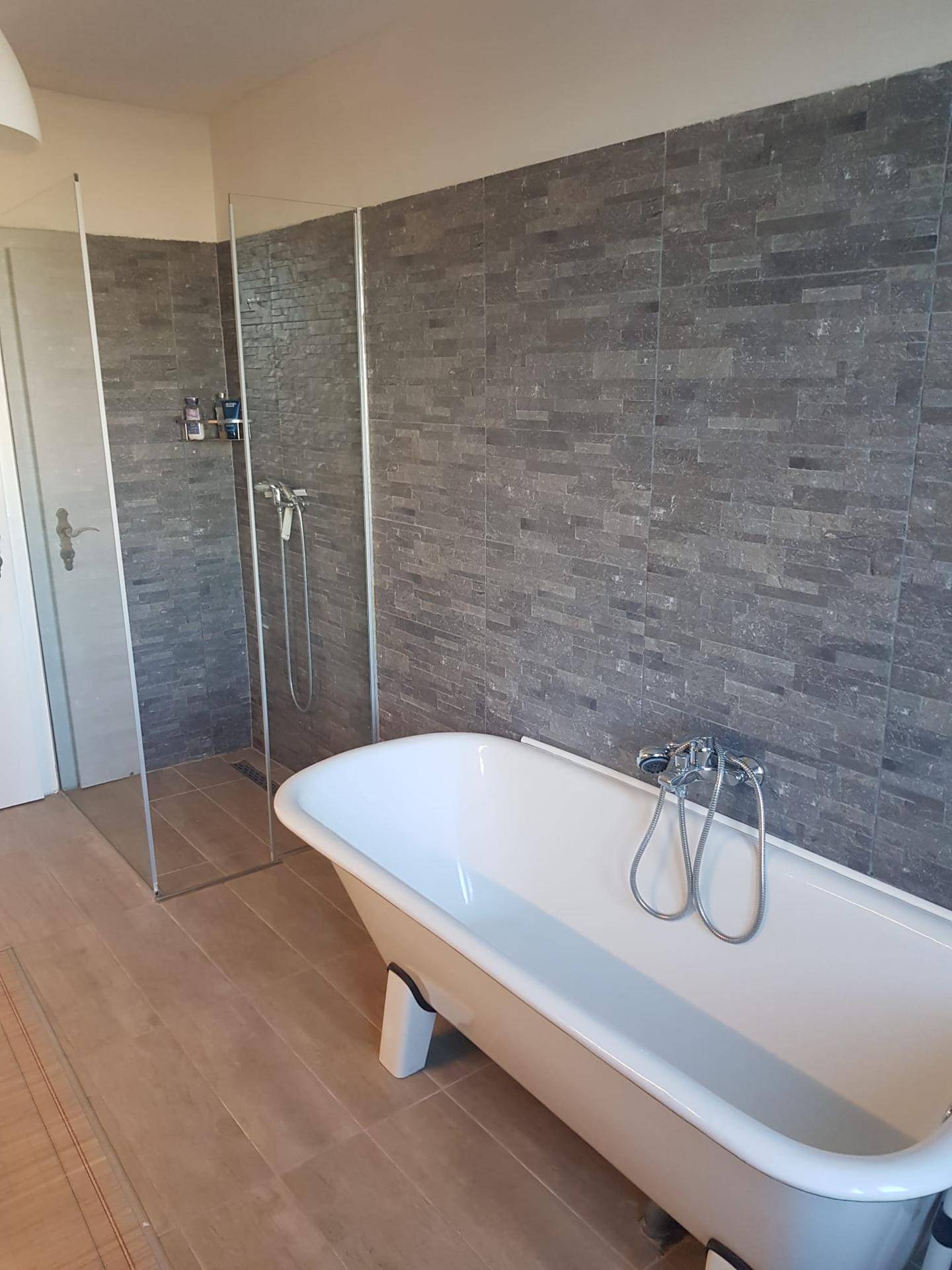 Geräumiges Badezimmer mit freistehender Badewanne und begehbarer Dusche mit Glasabtrennung.