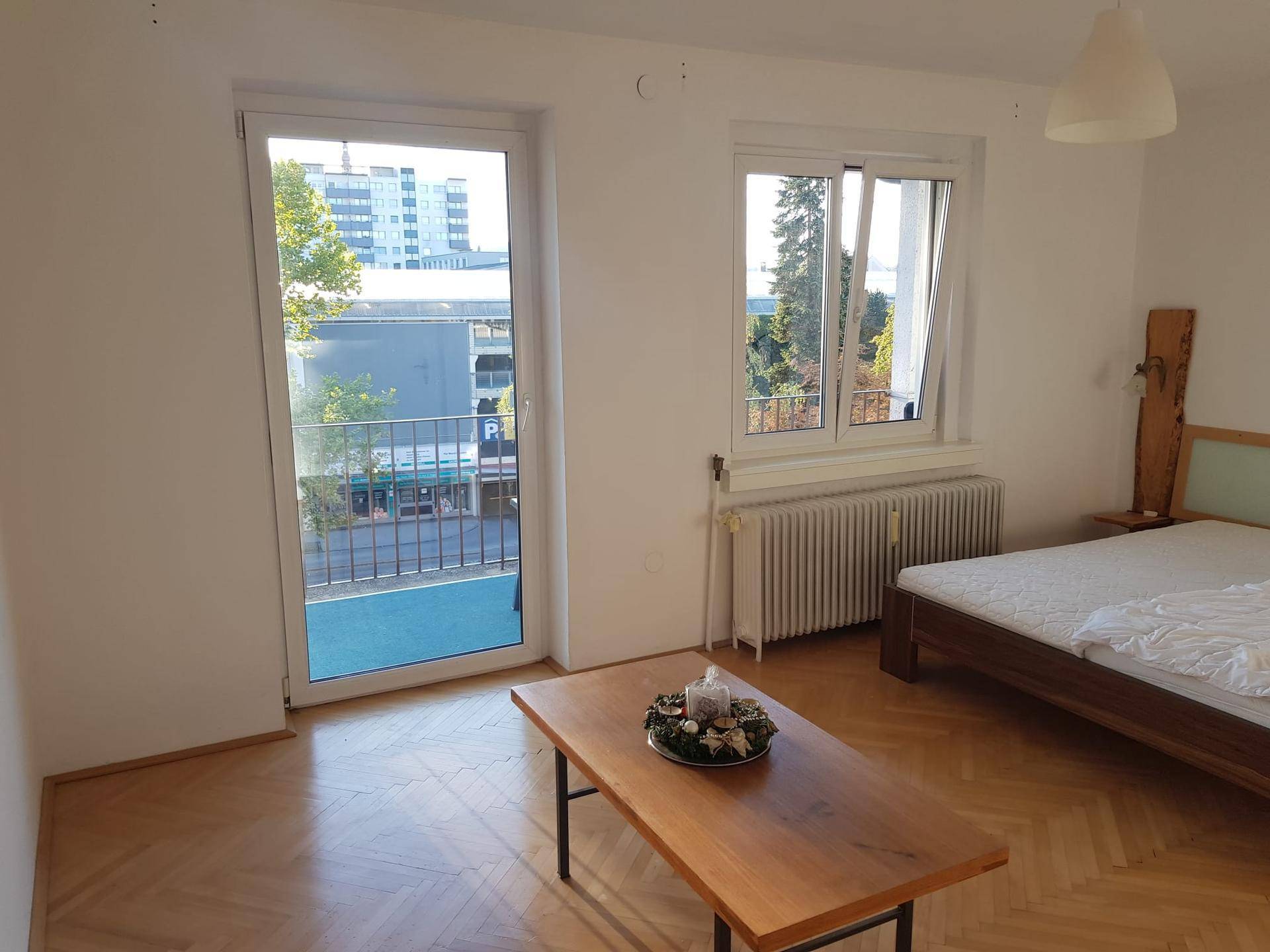 Gemütliches Schlafzimmer mit Fischgrätparkett, Bett und Zugang zu einem französischen Balkon.