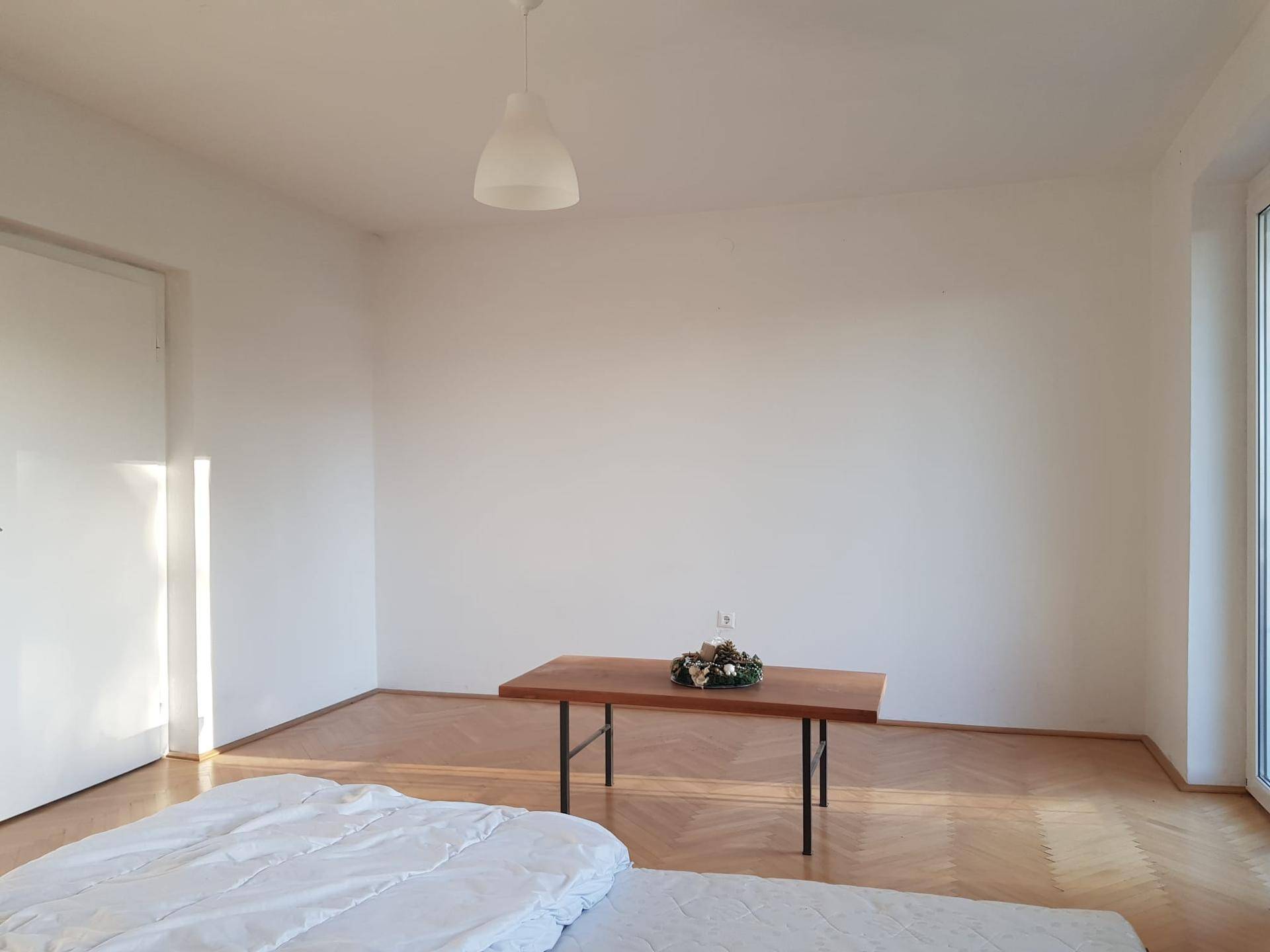 Helles Schlafzimmer mit Holzboden und einem großen Fenster, das viel Tageslicht hereinlässt.
