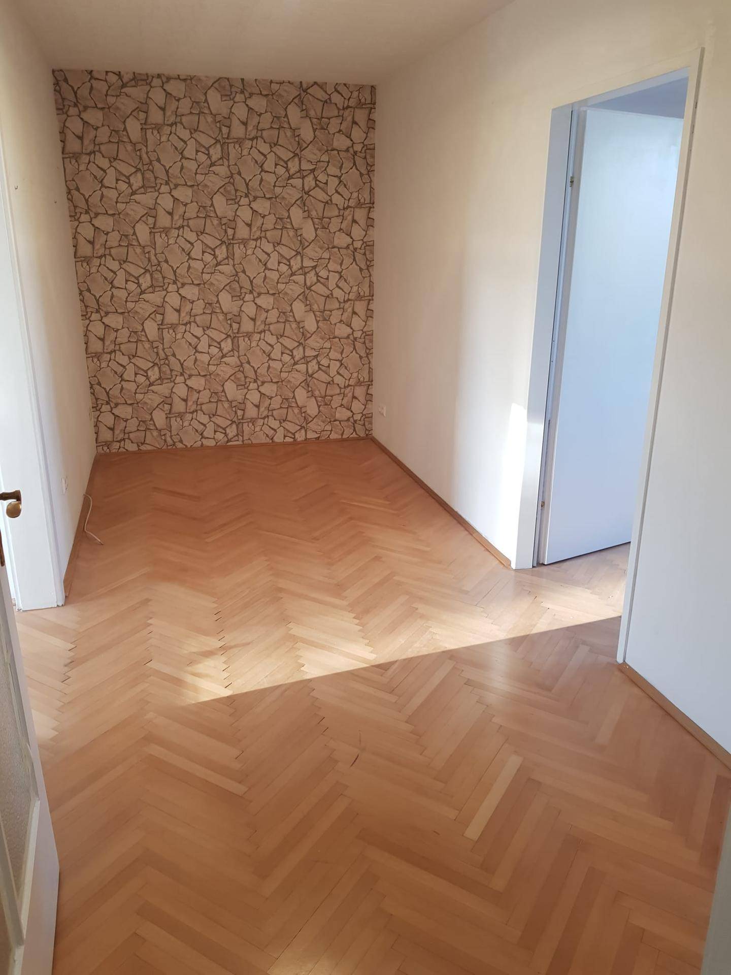 Helles Zimmer mit Fischgrätparkett und einer Akzentwand mit gemusterter Tapete.