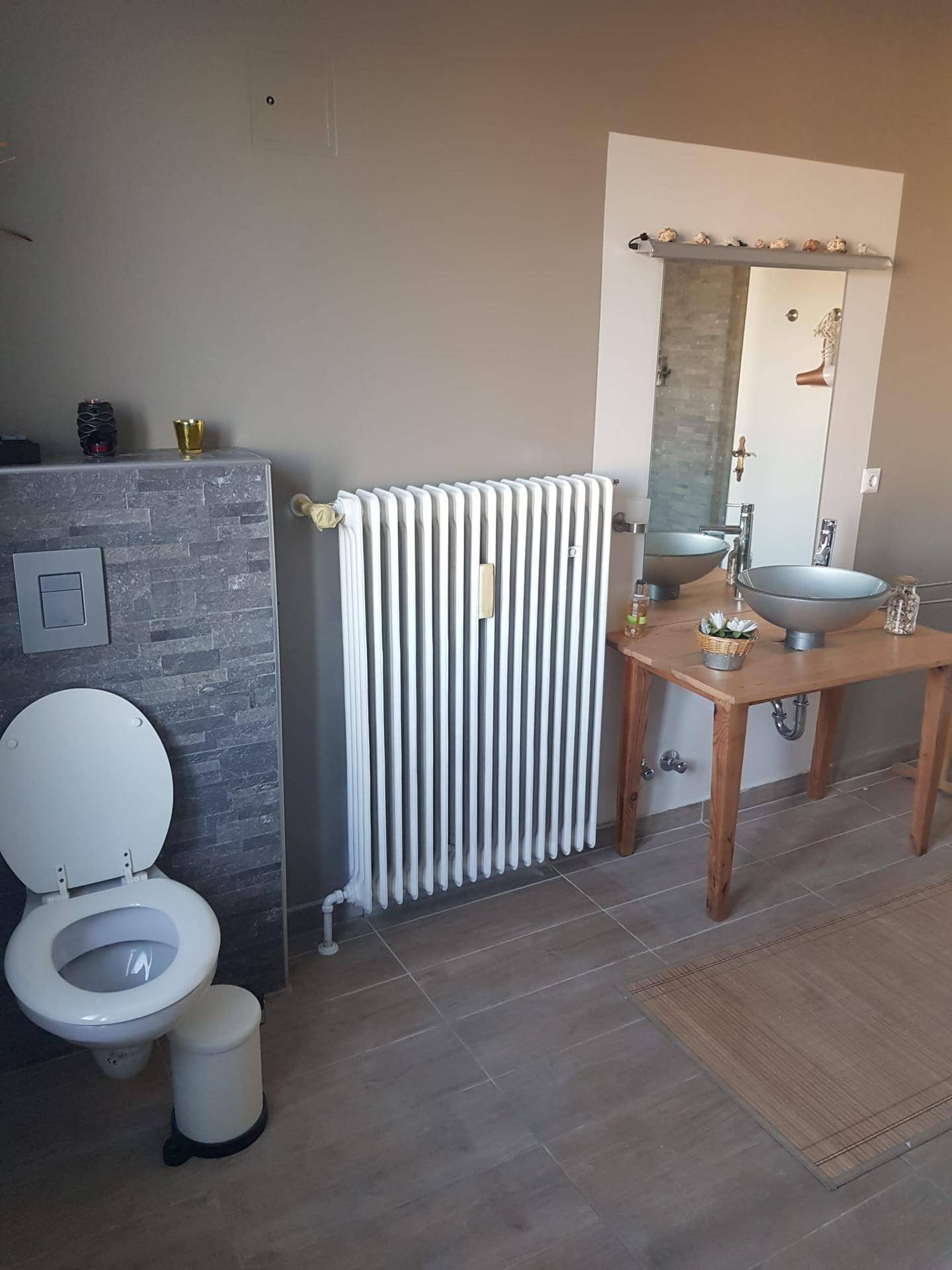 Modernes Badezimmer mit Wand-WC, Heizkörper und stilvollem Aufsatzwaschbecken auf Holztisch.