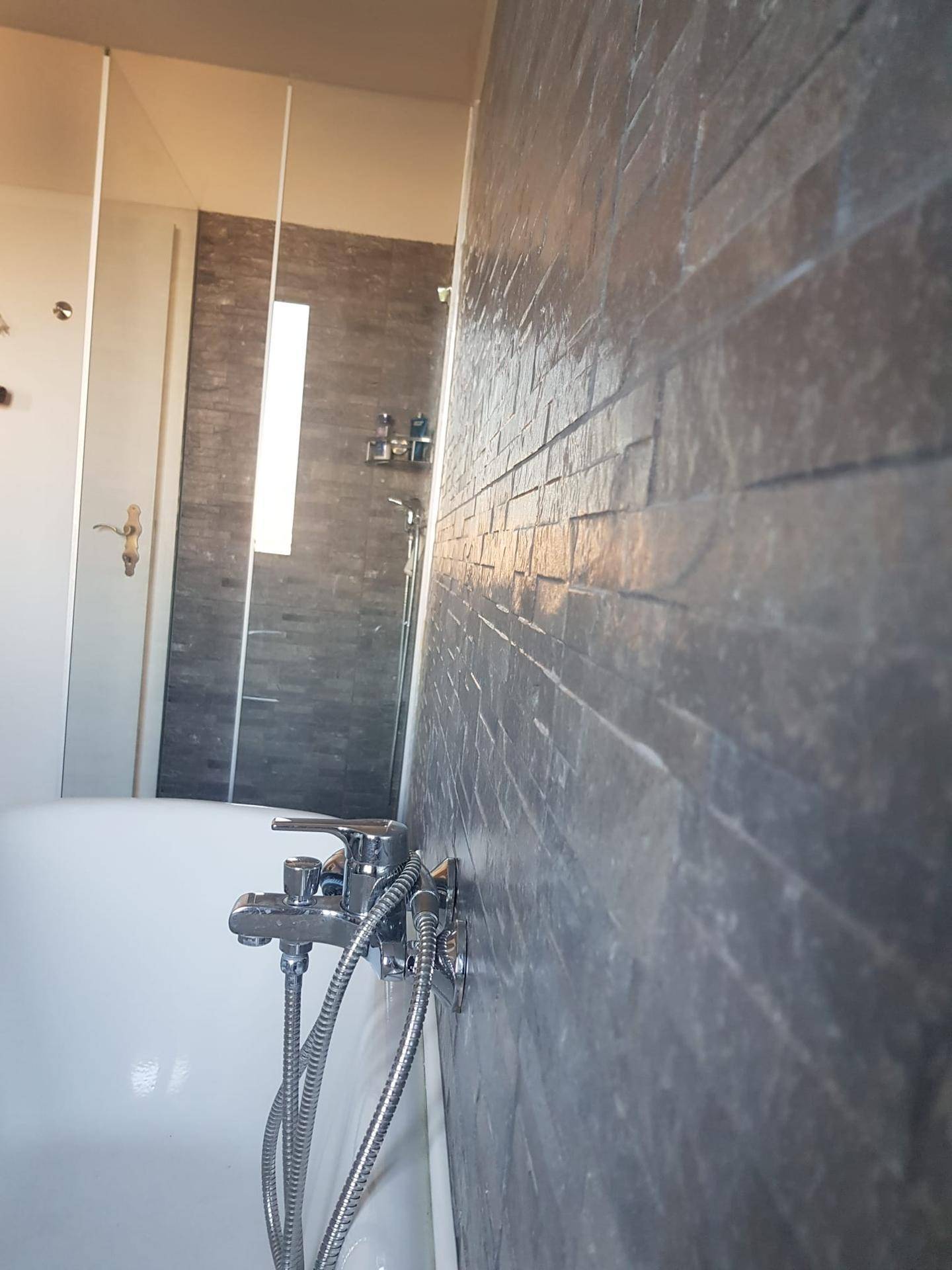 Detailaufnahme der Badewanne mit Armatur und moderner Schieferoptik-Fliesenwand im Badezimmer.