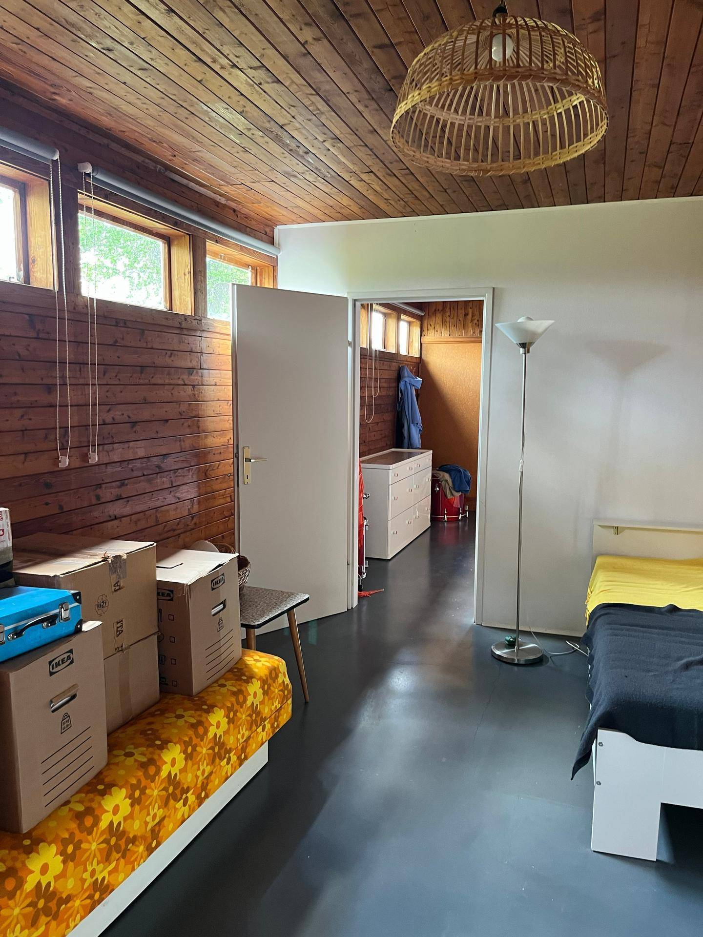 Schlafzimmer mit Holzwänden und -decke, Stauraum und Zugang zu einem weiteren Raum.