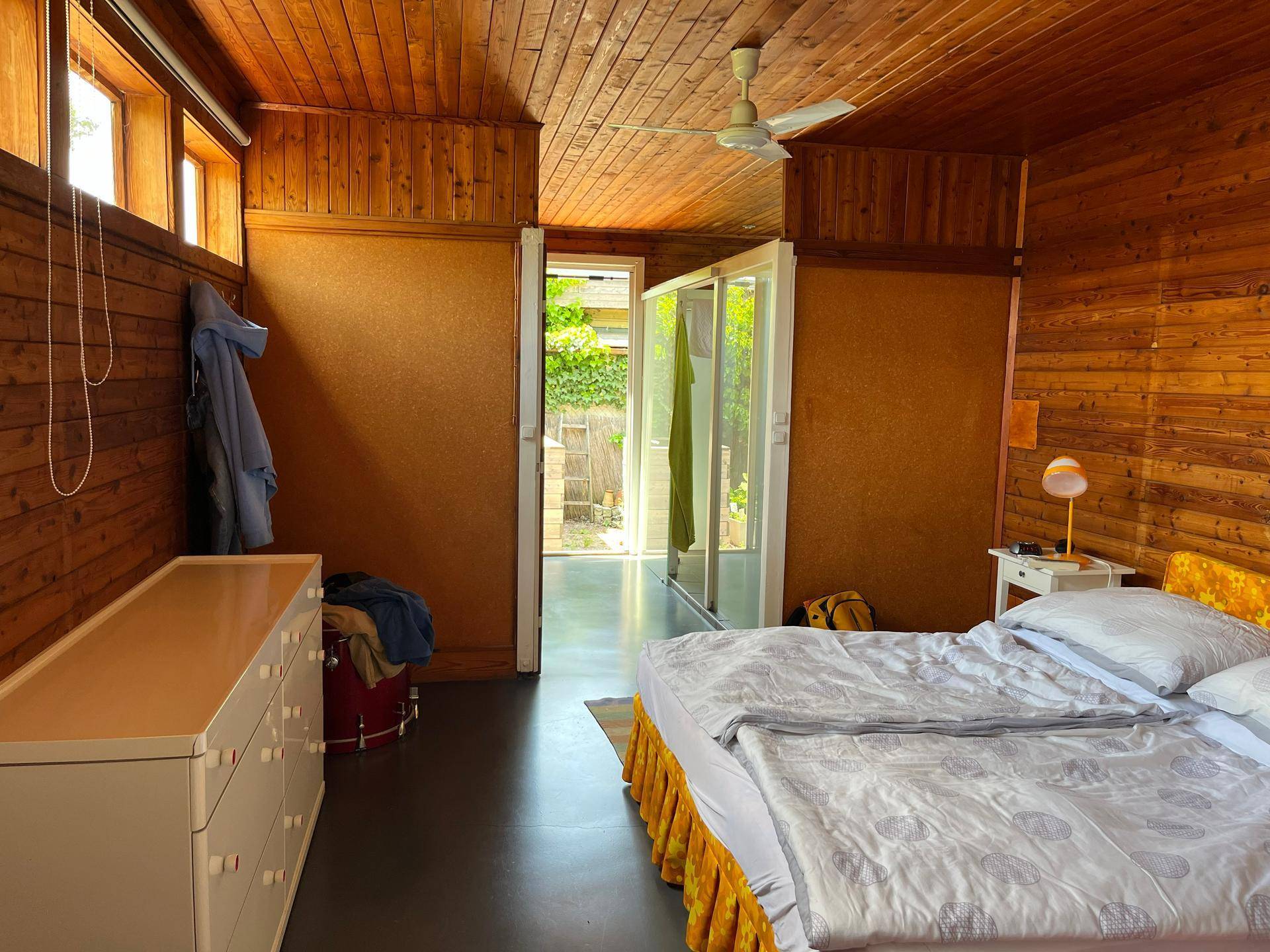 Schlafzimmer mit Holzwänden und -decke, dunklem Boden und Zugang zu einem weiteren Raum.