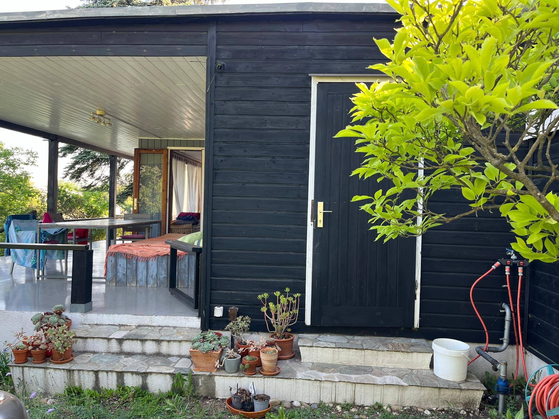 Schwarze Holzfassade des Hauses mit Zugang zur überdachten Terrasse und Gartenbereich.