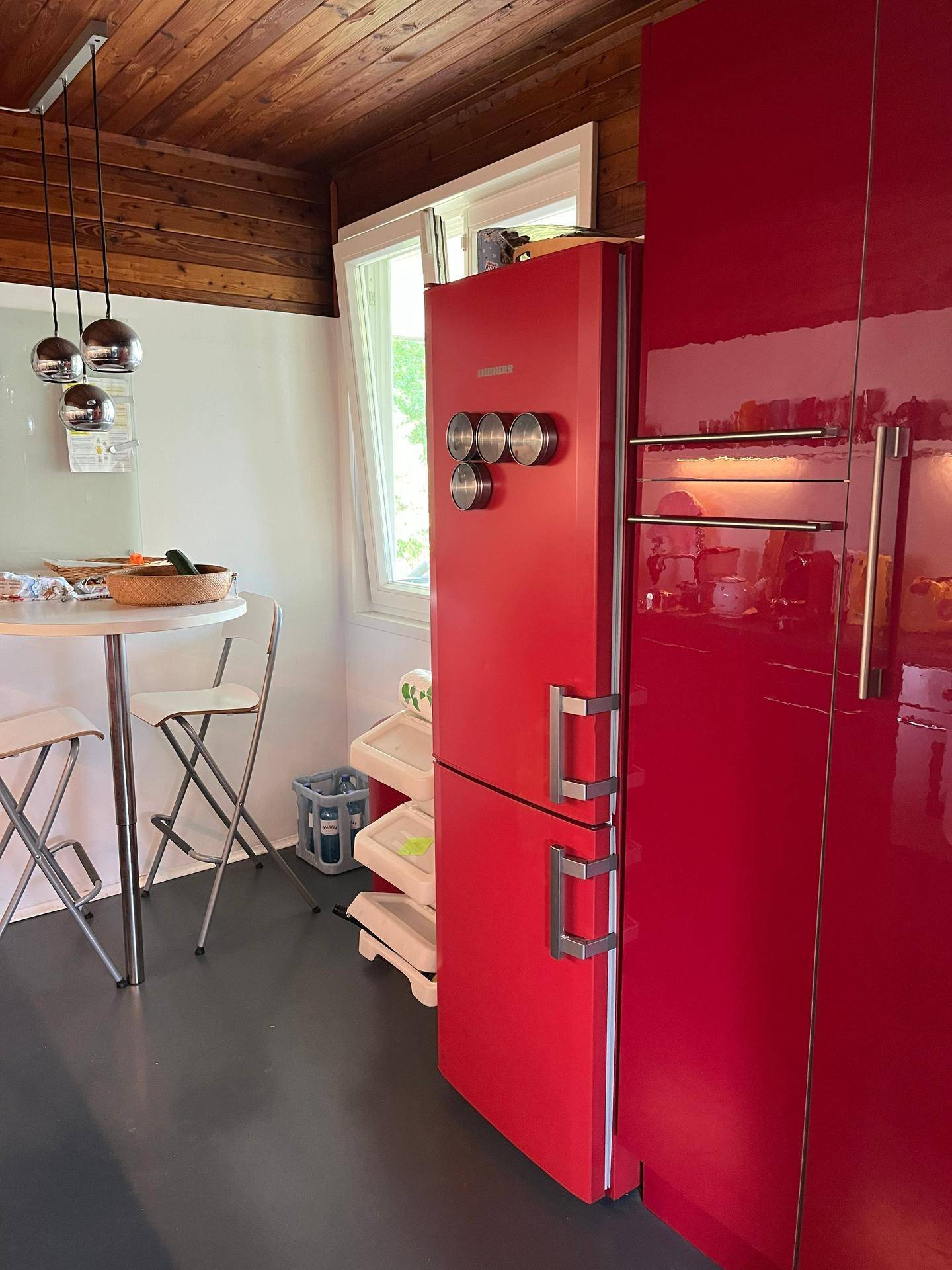 Roter Kühlschrank und passende Küchenschränke in einer modernen Küche mit Holzbalkendecke.