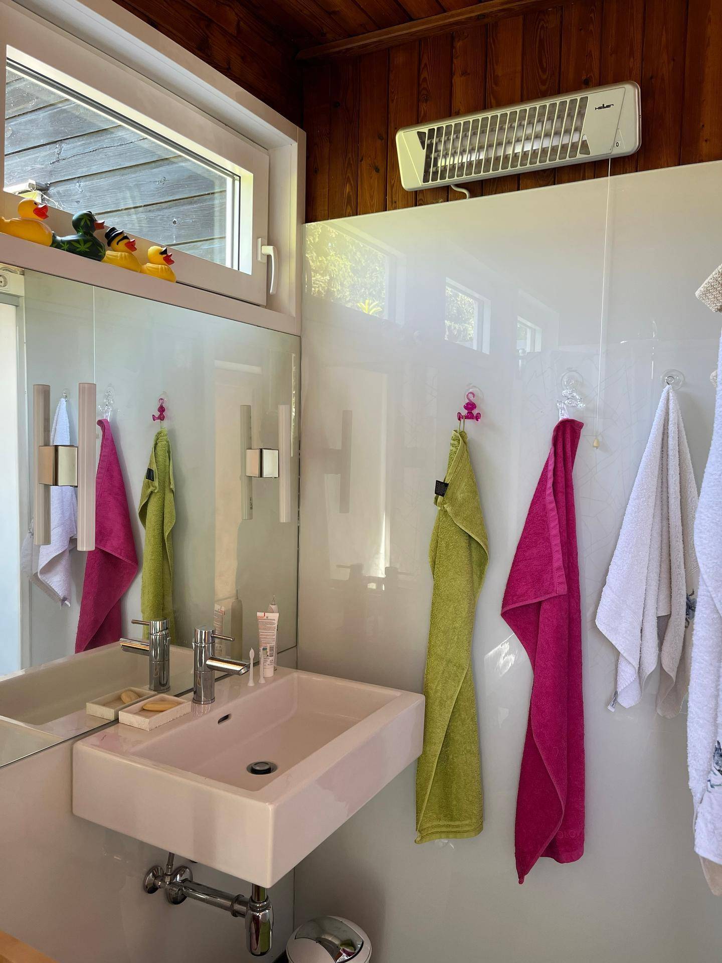 Badezimmer mit Einzelwaschbecken, Spiegel, bunten Handtüchern und Heizstrahler an der Wand.