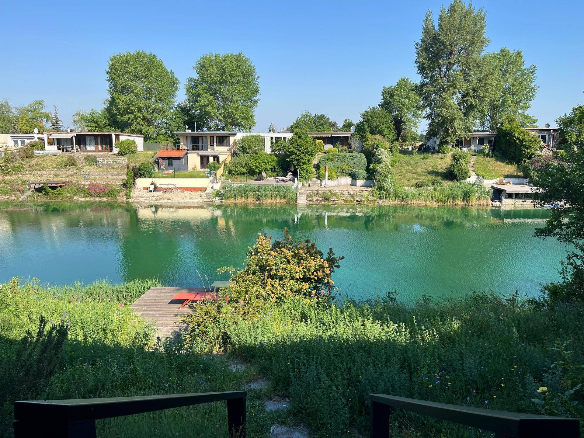 Malerischer Blick auf einen See mit gegenüberliegenden Häusern und üppiger Ufervegetation.
