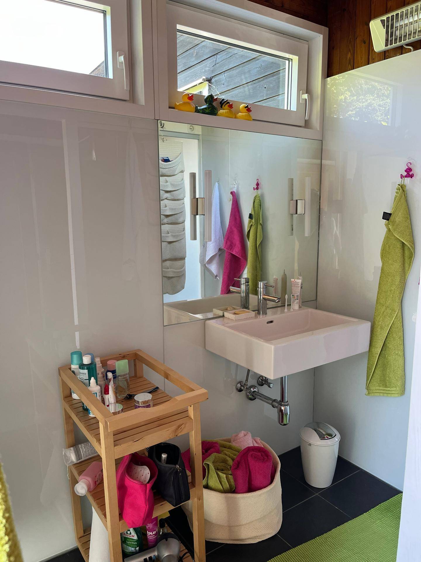 Modernes Badezimmer mit Einzelwaschbecken, Spiegel und Fenster für natürliches Licht.