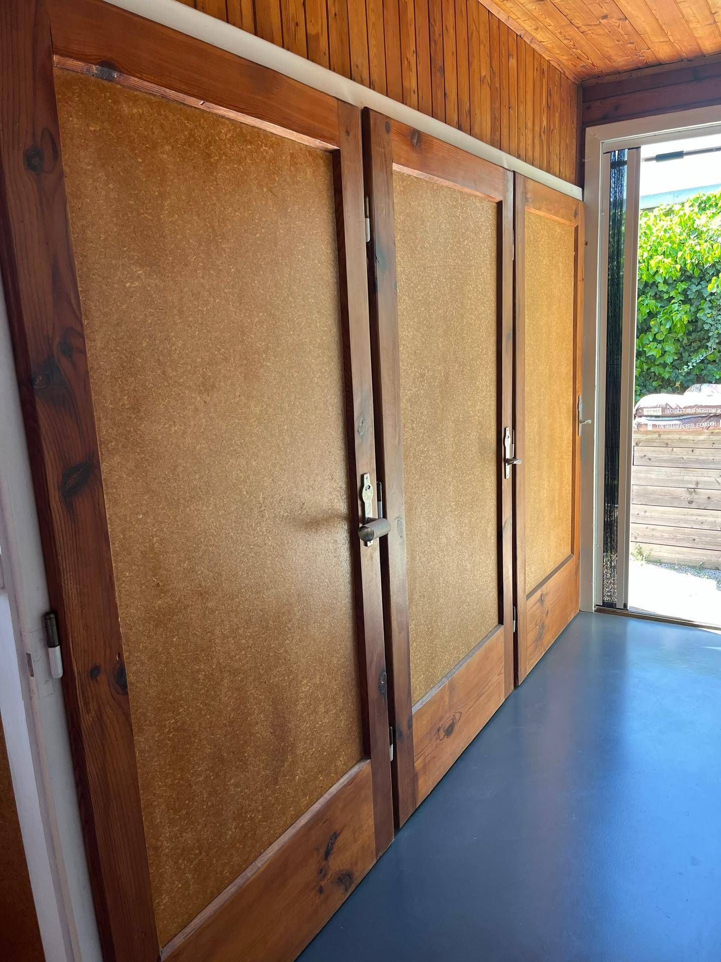 Holzvertäfelte Wand mit mehreren Türen und Zugang zu einem Außenbereich.
