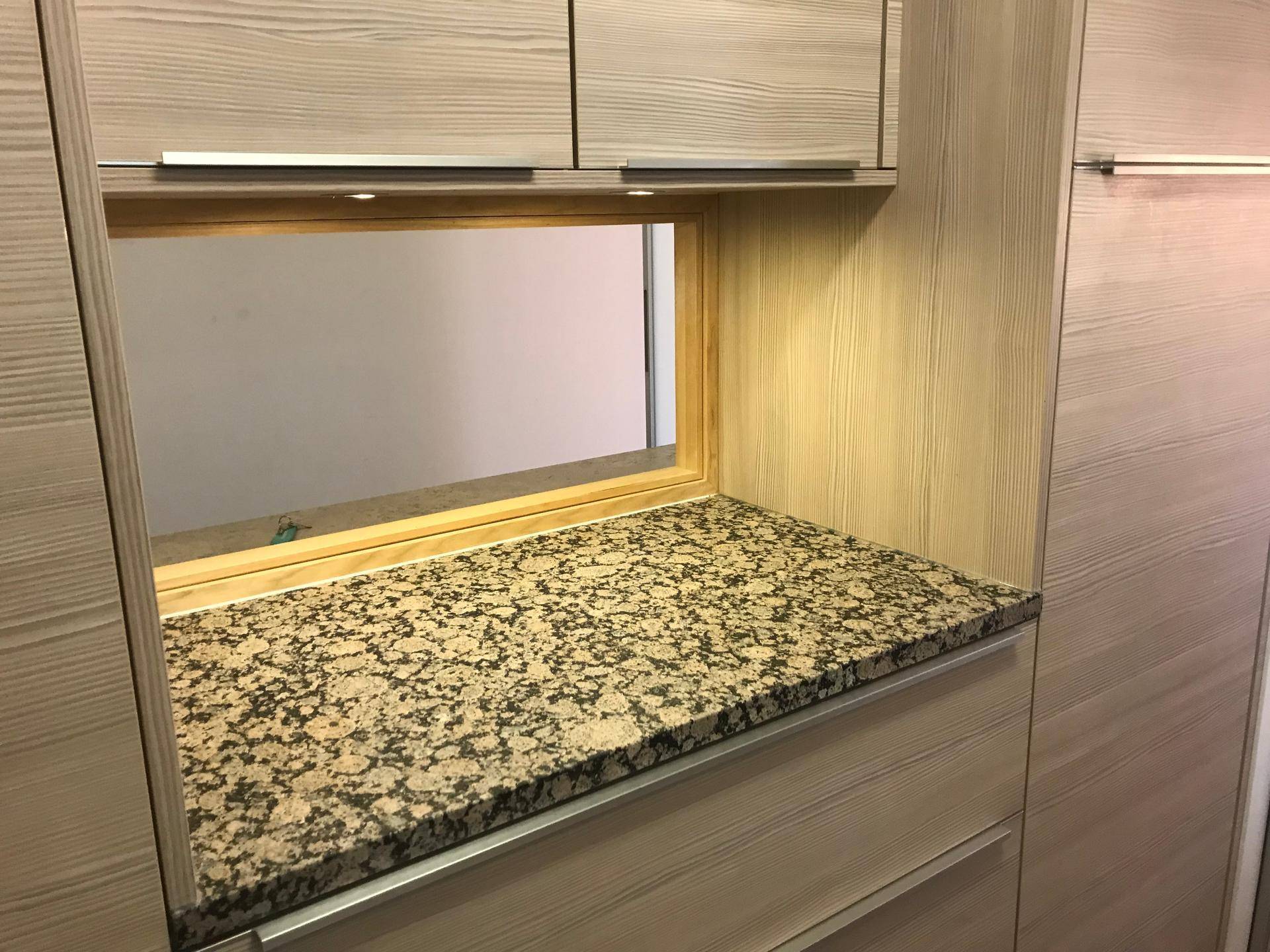 Detailansicht einer Küchen-Durchreiche mit Granitarbeitsplatte und Holzverkleidung.
