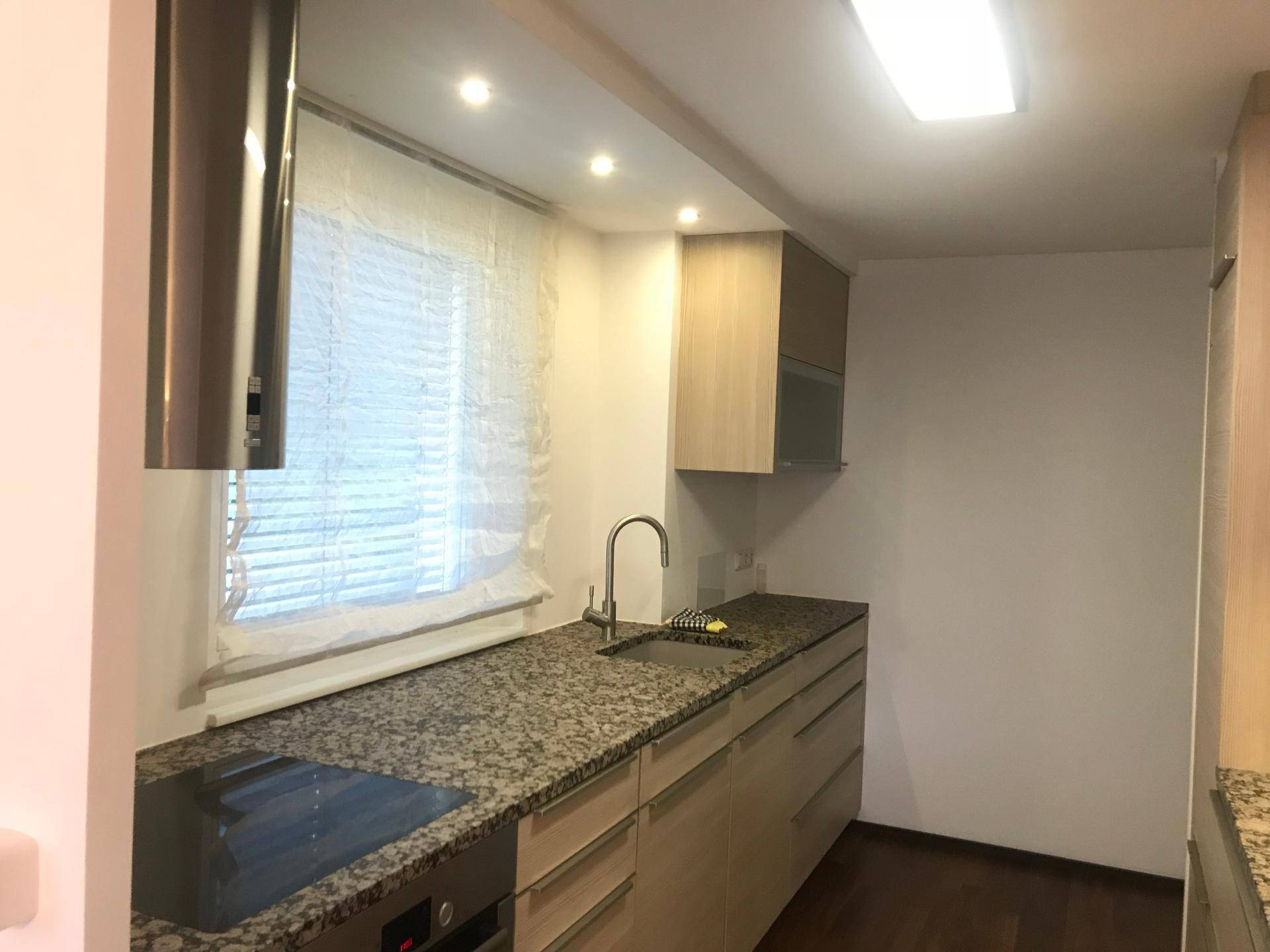 Funktionale Küche mit Induktionskochfeld, Spüle und Granitarbeitsplatte unter einem Fenster.