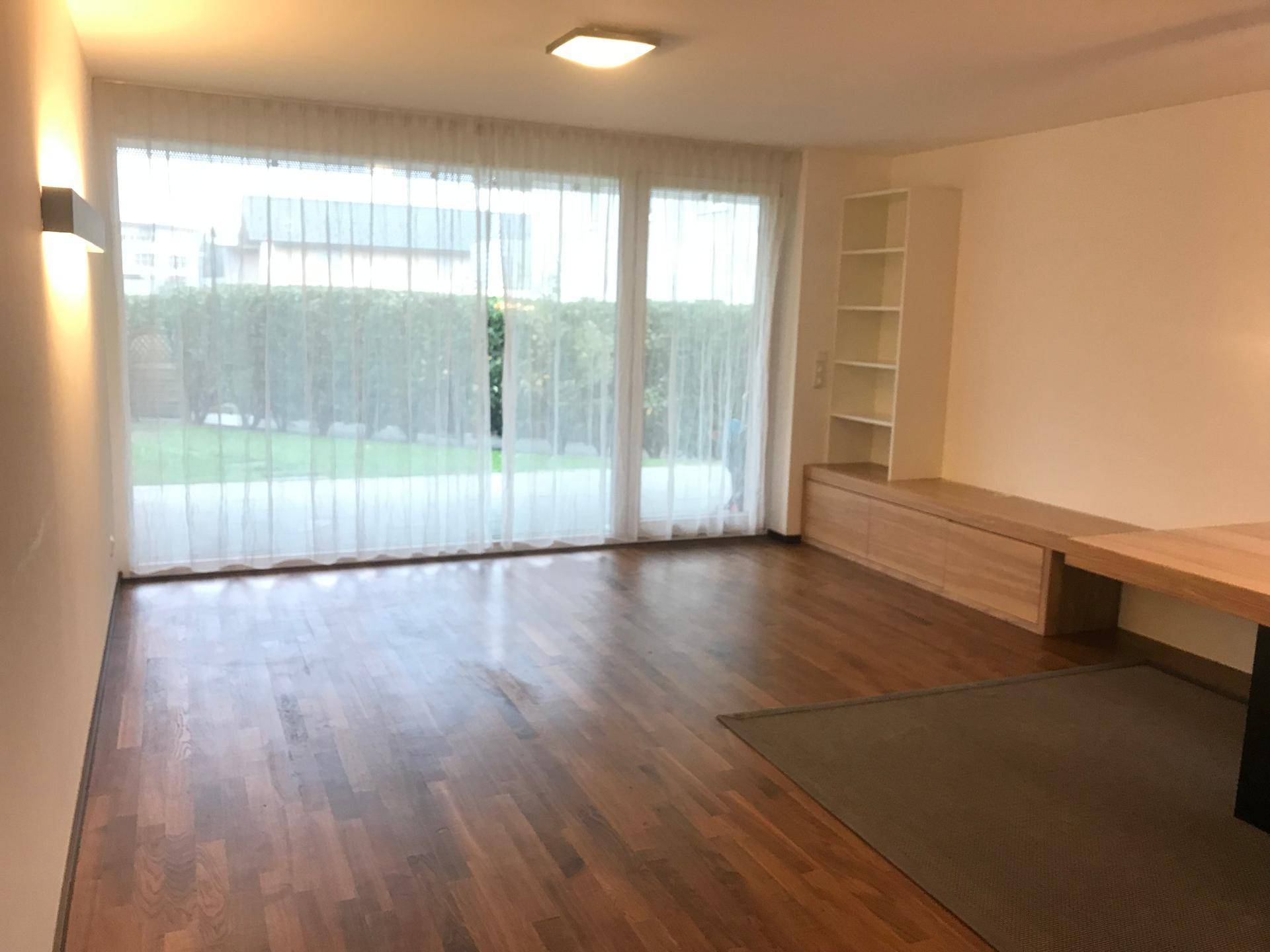 Helles Wohnzimmer mit großen Glasfronten zum Garten und elegantem Parkettboden.