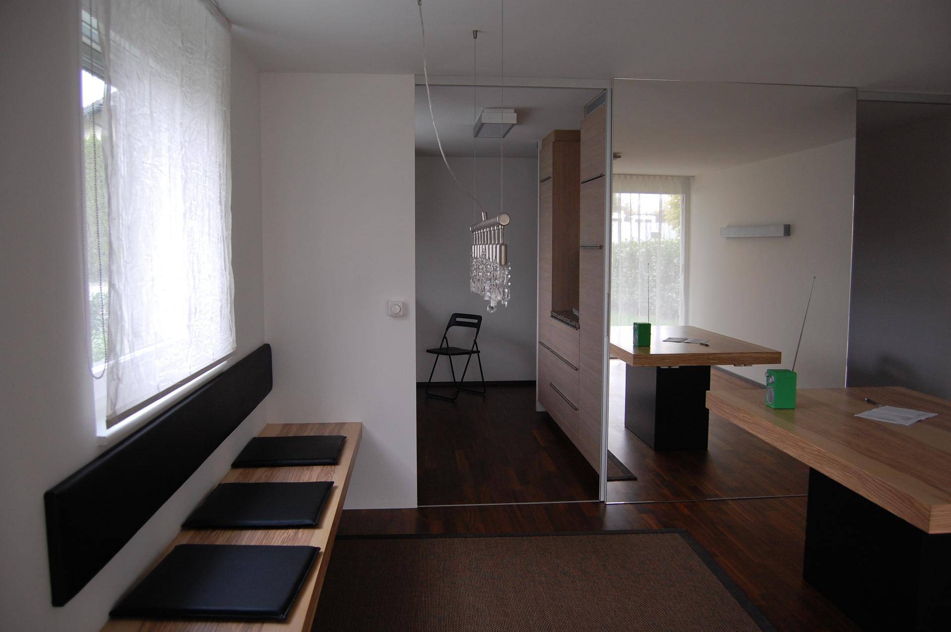Essbereich mit Holztisch und Sitzbank, durch eine Spiegelfläche optisch erweitert und hell.