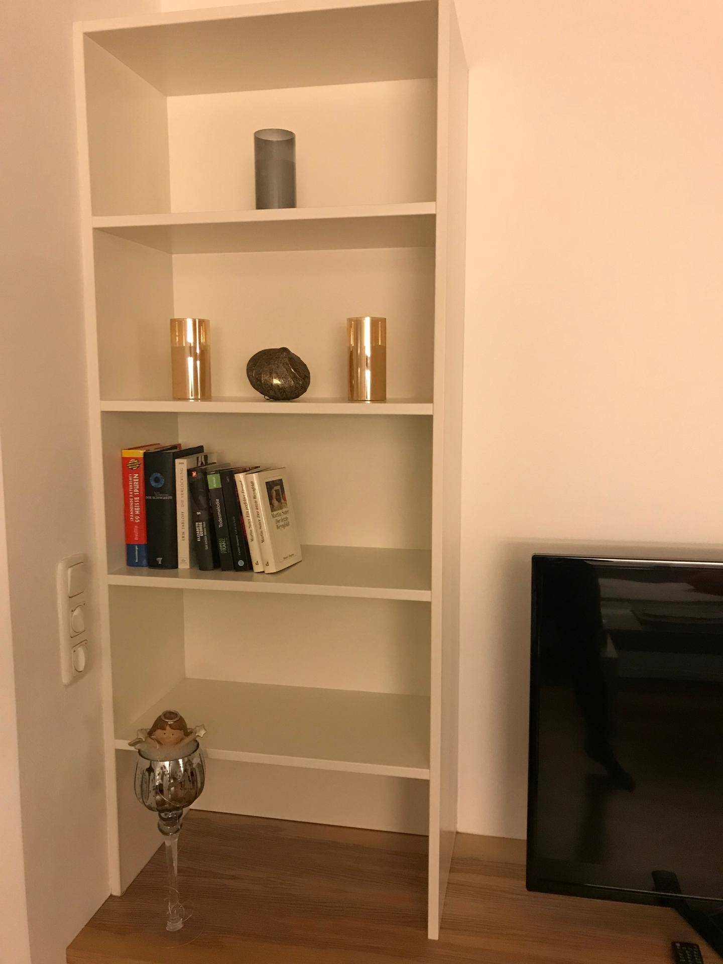 Weißes Bücherregal mit Büchern und dekorativen Elementen, Teil des Wohnbereichs.
