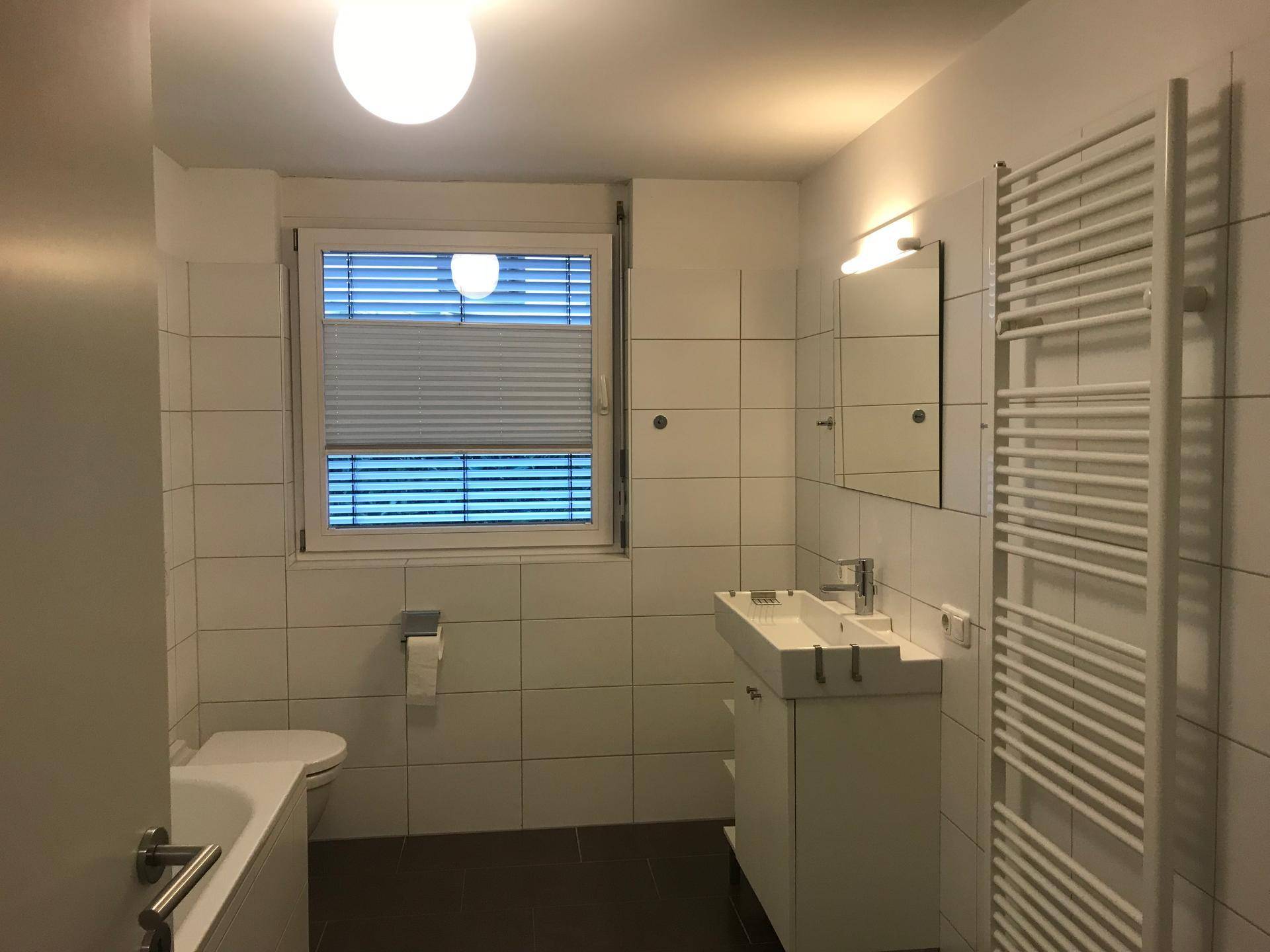 Modernes Badezimmer mit weißen Fliesen, WC, Waschbecken und beheiztem Handtuchhalter.
