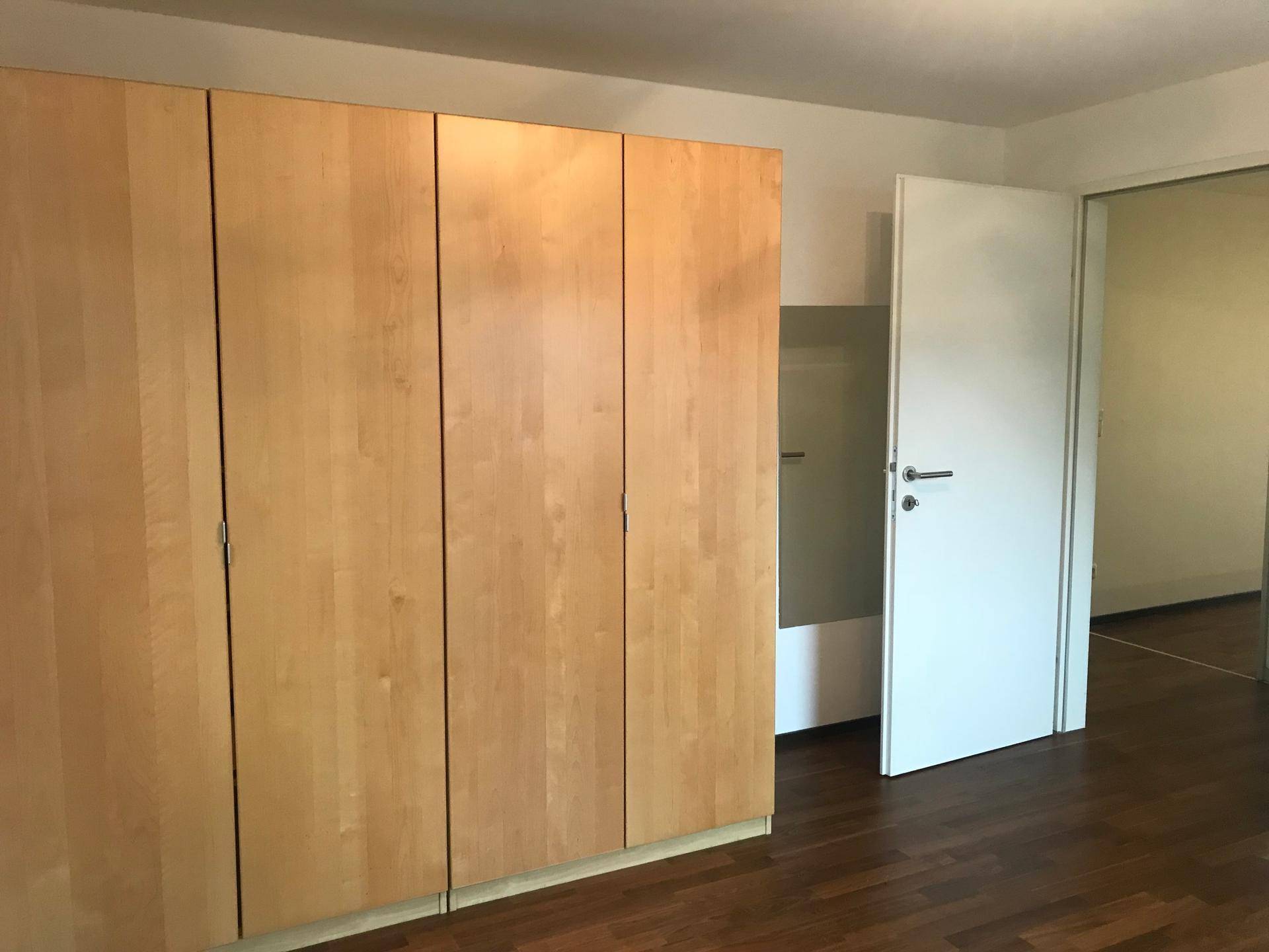 Schlafzimmer mit großem Holzschrank und elegantem Parkettboden, bietet viel Stauraum.