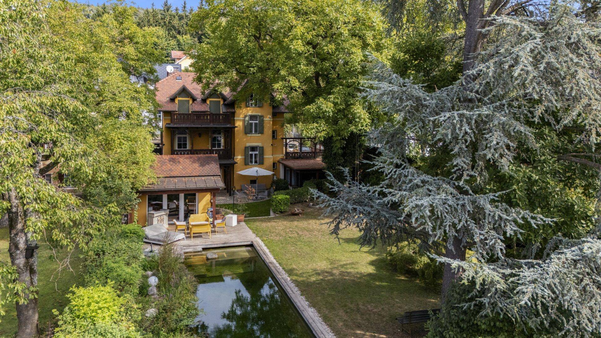 Luftaufnahme der Villa mit großem Garten, Teich und altem Baumbestand.