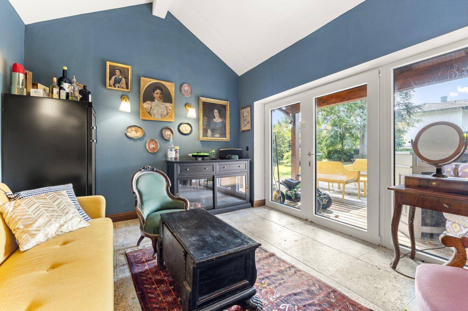 Wohnzimmer mit Zugang zum Garten, hohen Decken und antiken Gemälden an der Wand.