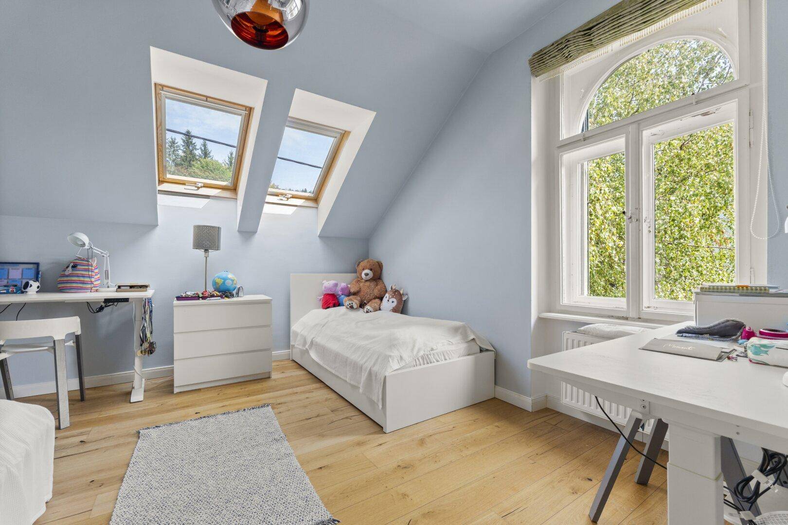Helles Schlafzimmer im Dachgeschoss mit Dachfenstern und Holzboden.
