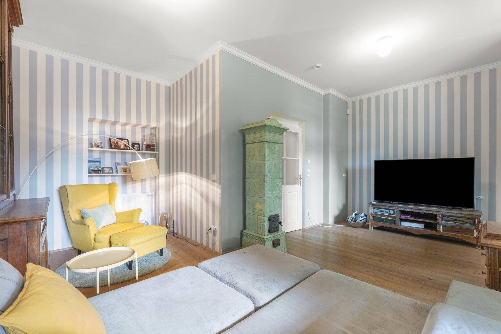 Gemütliches Wohnzimmer mit Kachelofen, gestreiften Wänden und großem Fernseher.