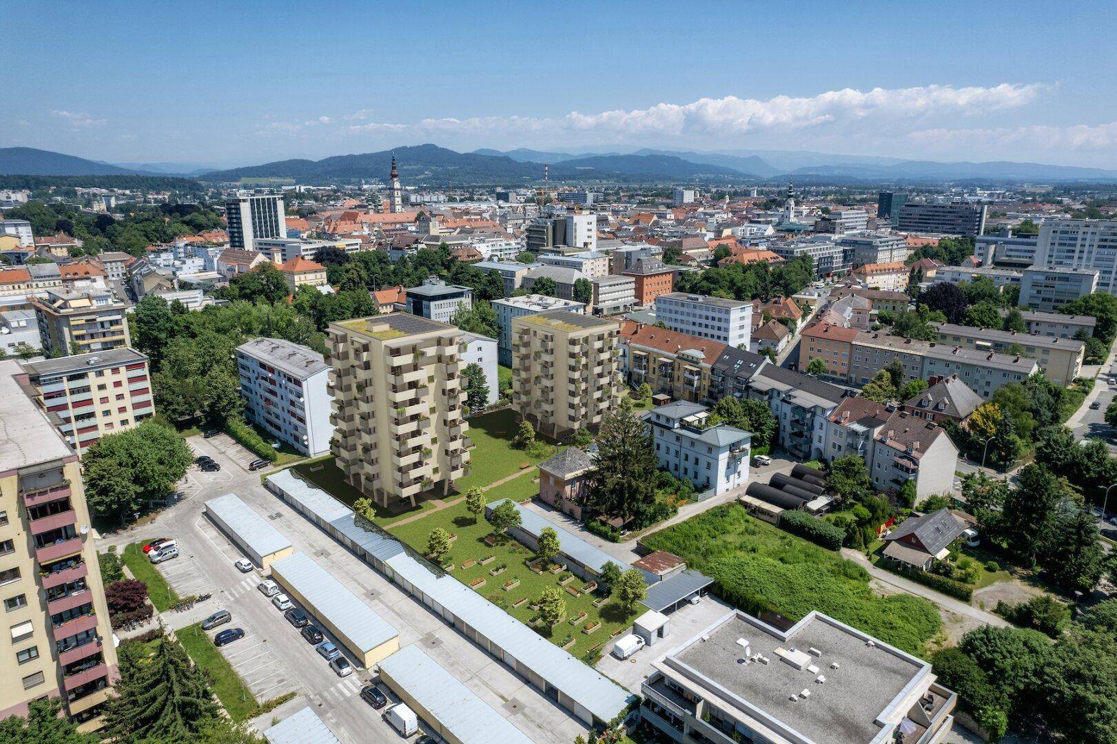 Luftaufnahme der Wohngebäude im städtischen Umfeld mit Blick auf die umliegende Bebauung und Berge im Hintergrund.