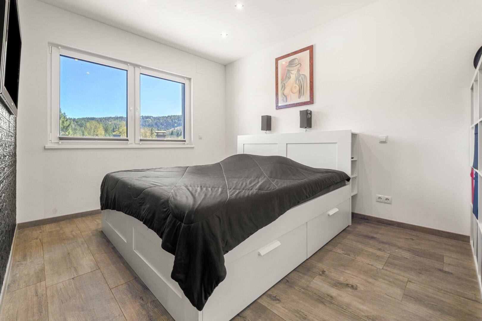Schlafzimmer mit großem Fenster, Holzbodenoptik und Blick ins Grüne.
