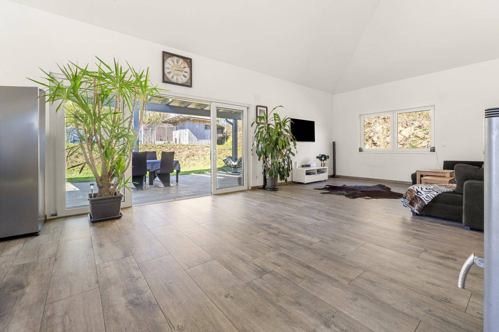 Helles Wohnzimmer mit Holzoptik-Fliesenboden und Zugang zur Terrasse mit Gartenblick.