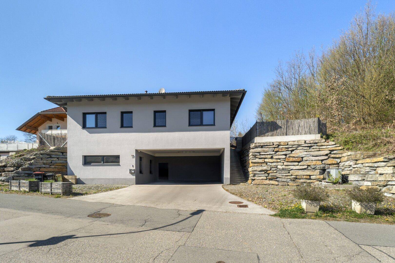 Modernes Wohnhaus mit integriertem Carport und Natursteinmauer am Hang.