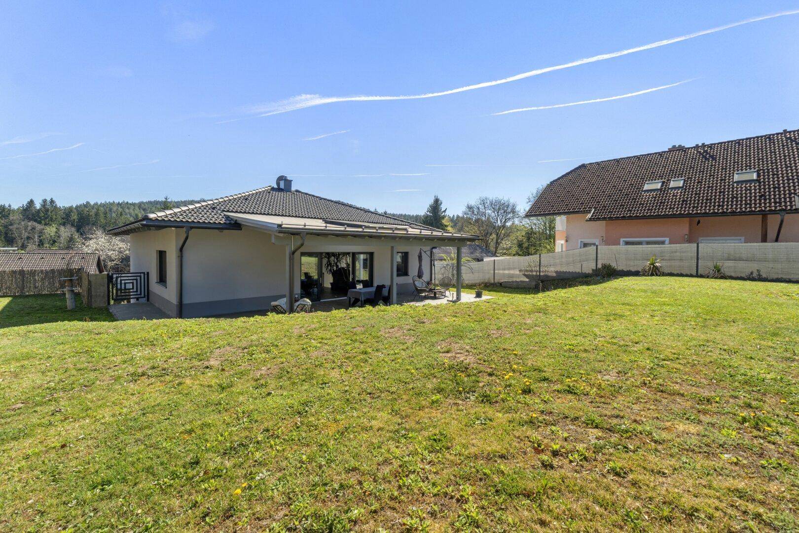Modernes Einfamilienhaus mit großer Rasenfläche und überdachter Terrasse im Grünen.