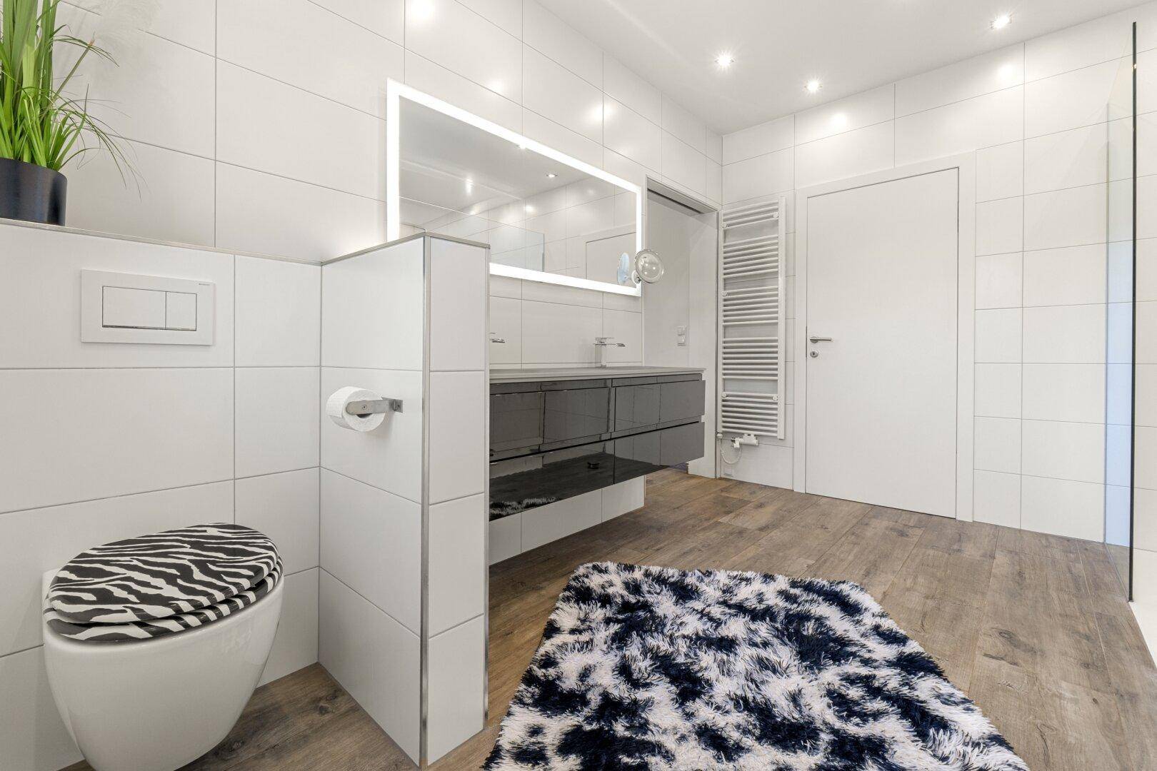 Helles Badezimmer mit modernem Waschtisch, beleuchtetem Spiegel und Heizkörper.