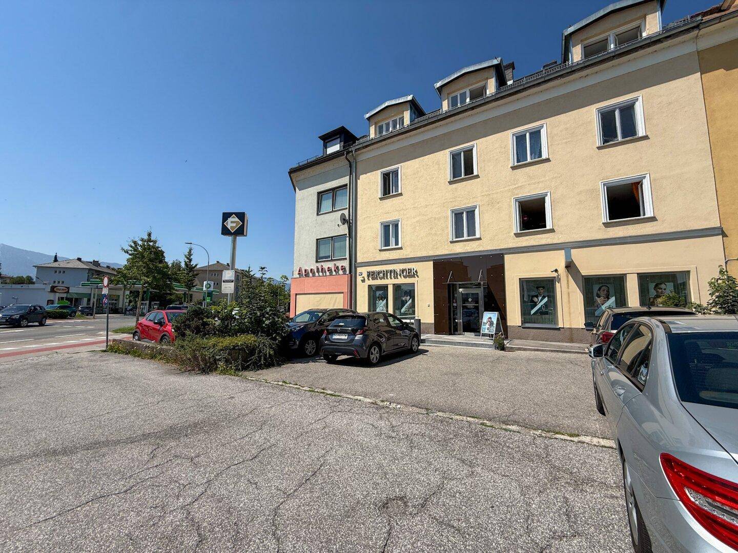 Eine Ansicht des Gebäudes von der Straße aus, mit geparkten Autos und Geschäften im Erdgeschoss.