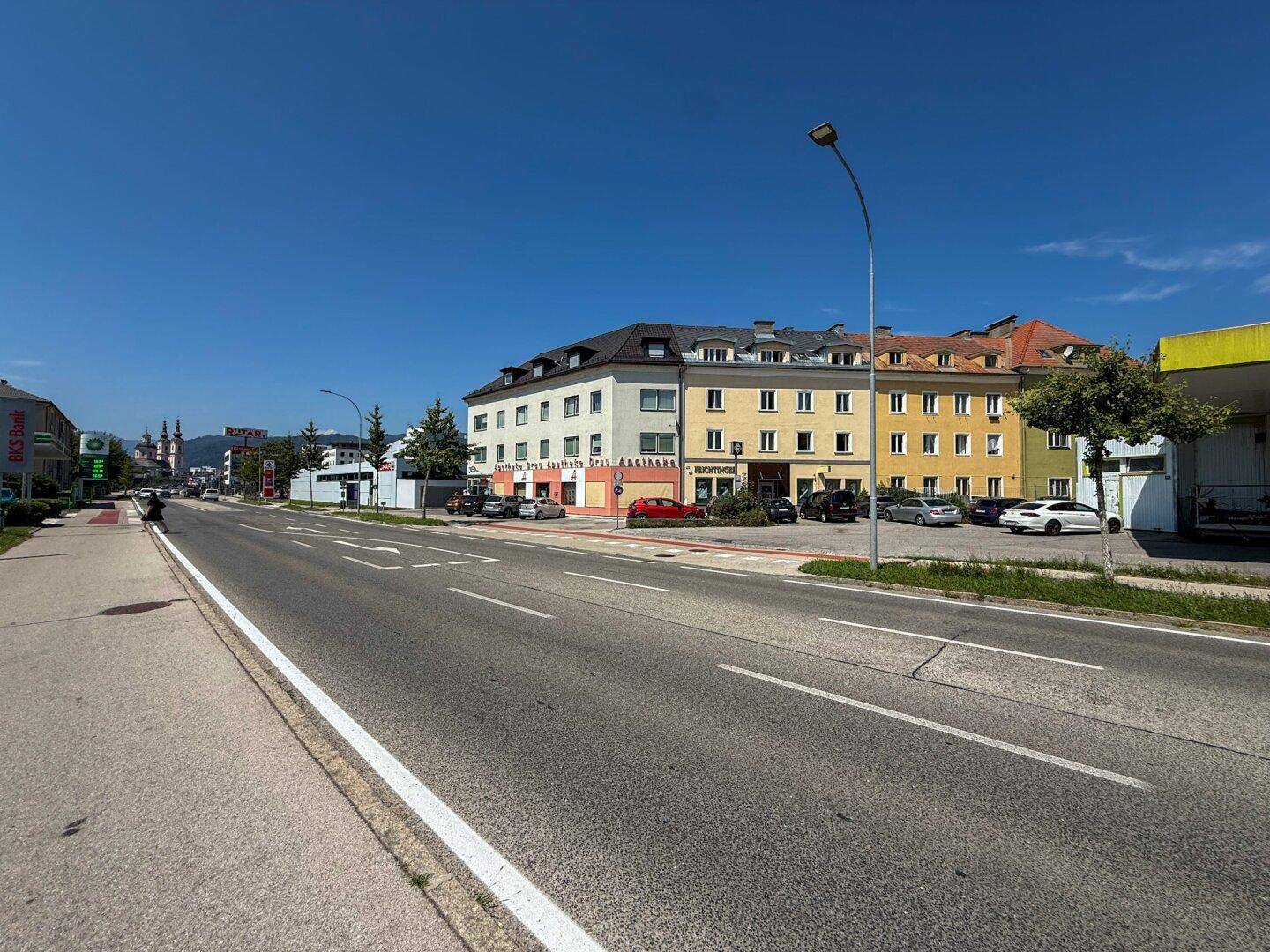Eine lange Straßenansicht mit dem Gebäude in der Ferne und anderen Geschäften entlang der Straße.