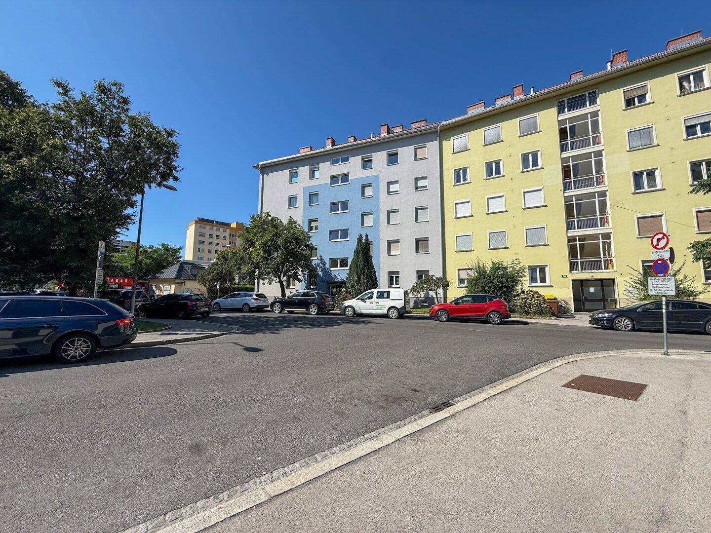 Wohngebäude mit farbigen Fassaden und parkenden Autos an einer ruhigen Straße.