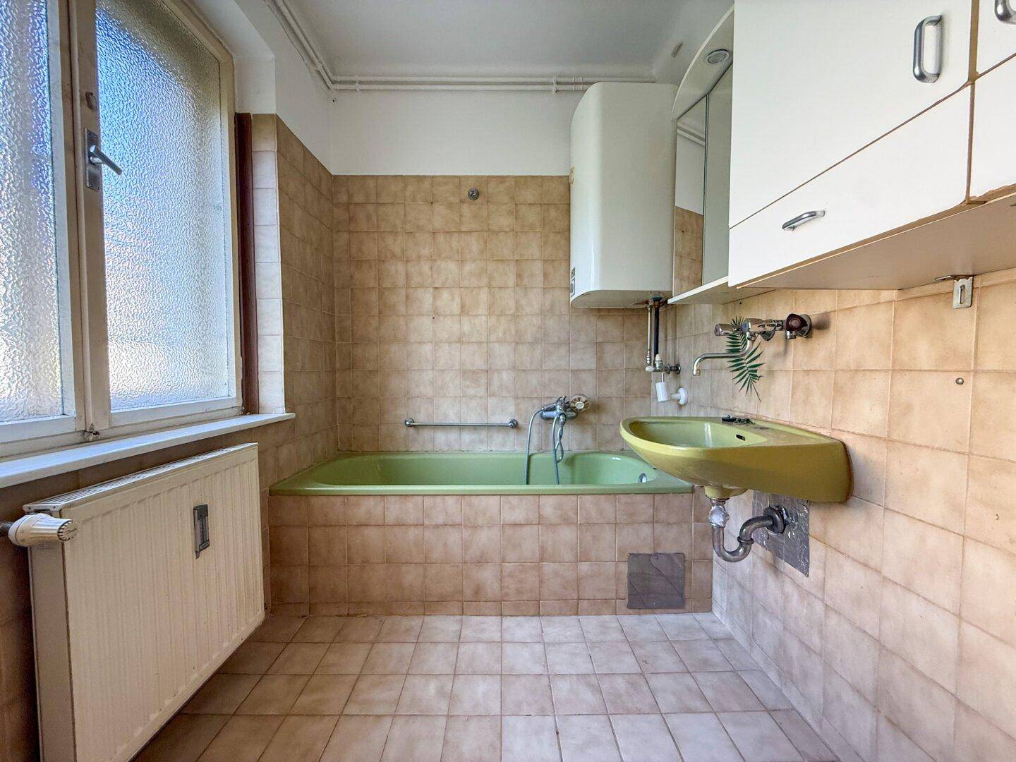 Badezimmer im 80er-Jahre-Stil mit grüner Badewanne, gelbem Waschbecken und Fliesen an den Wänden.