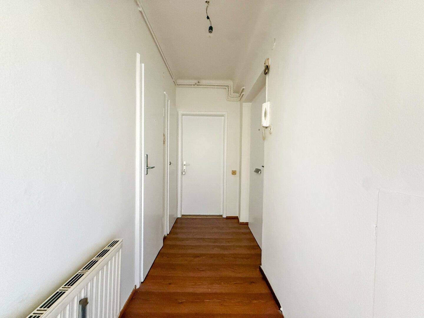 Heller Flur mit Holzboden und mehreren Türen, der zu verschiedenen Räumen führt.