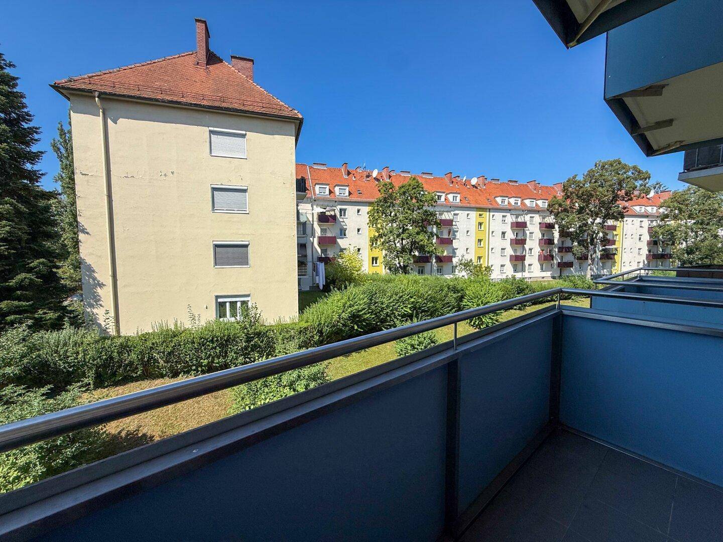 Balkon mit Blick auf die umliegenden Wohngebäude und grüne Bepflanzung.