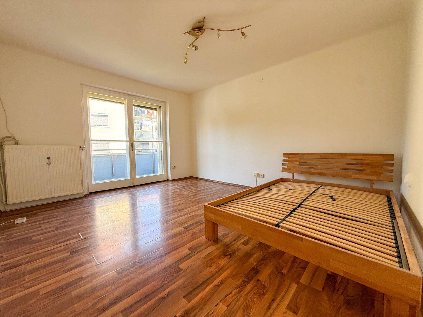 Schlafzimmer mit Holzboden und Zugang zu einem französischen Balkon, bereit zur Einrichtung.