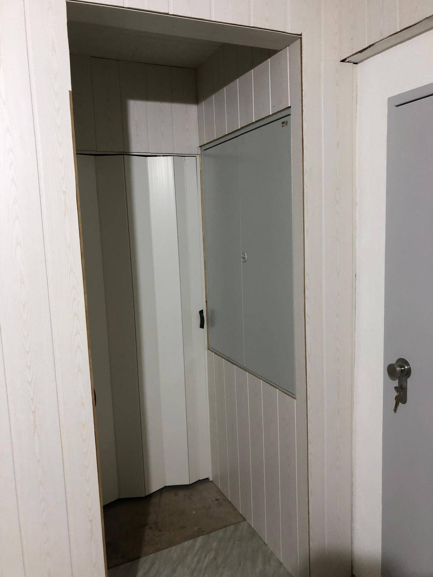 Schmaler Abstellraum mit weißer Holzverkleidung und einer Falttür.