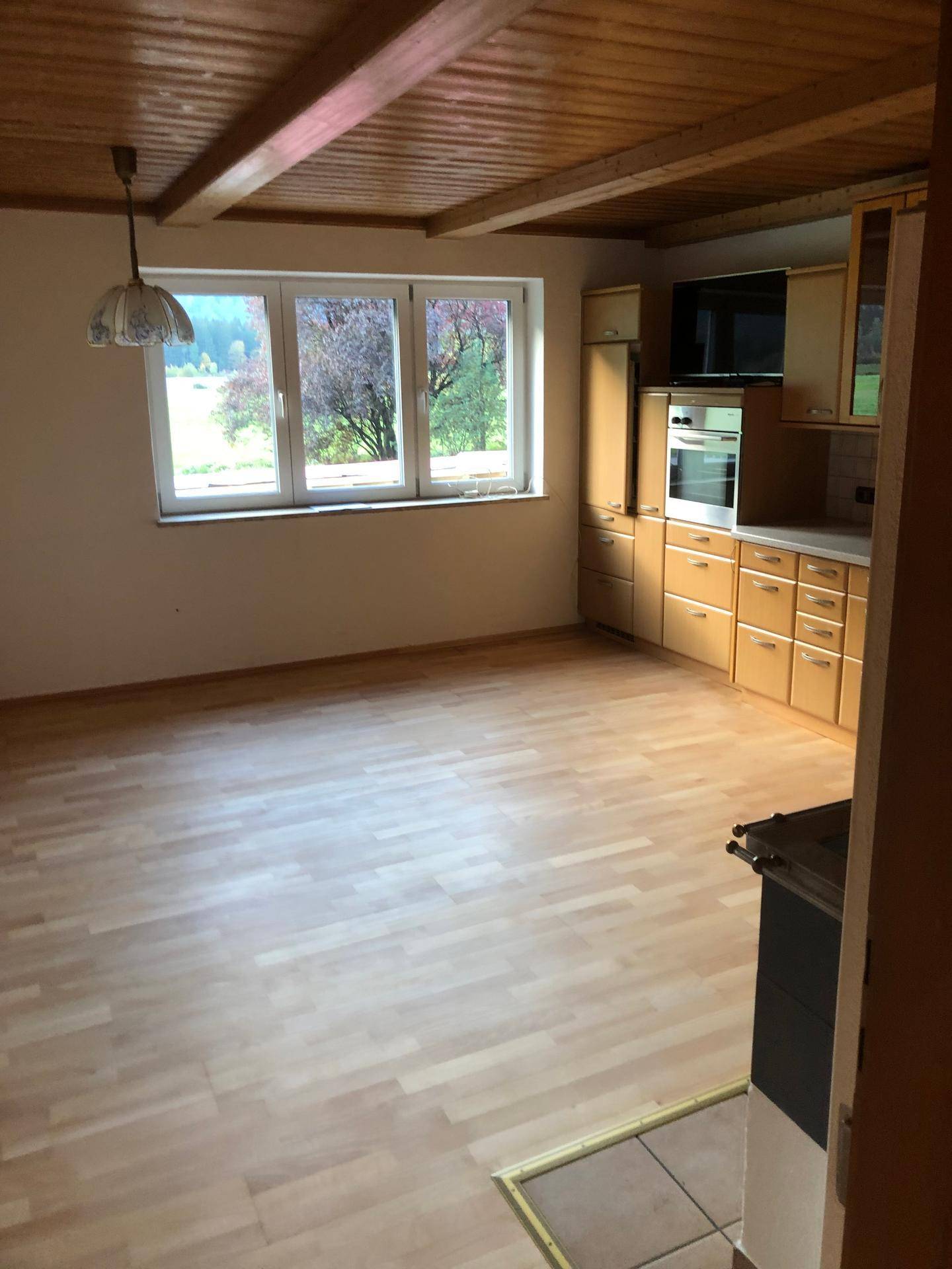 Geräumige Küche mit Holzbalkendecke, Laminatboden und Blick ins Grüne durch große Fenster.