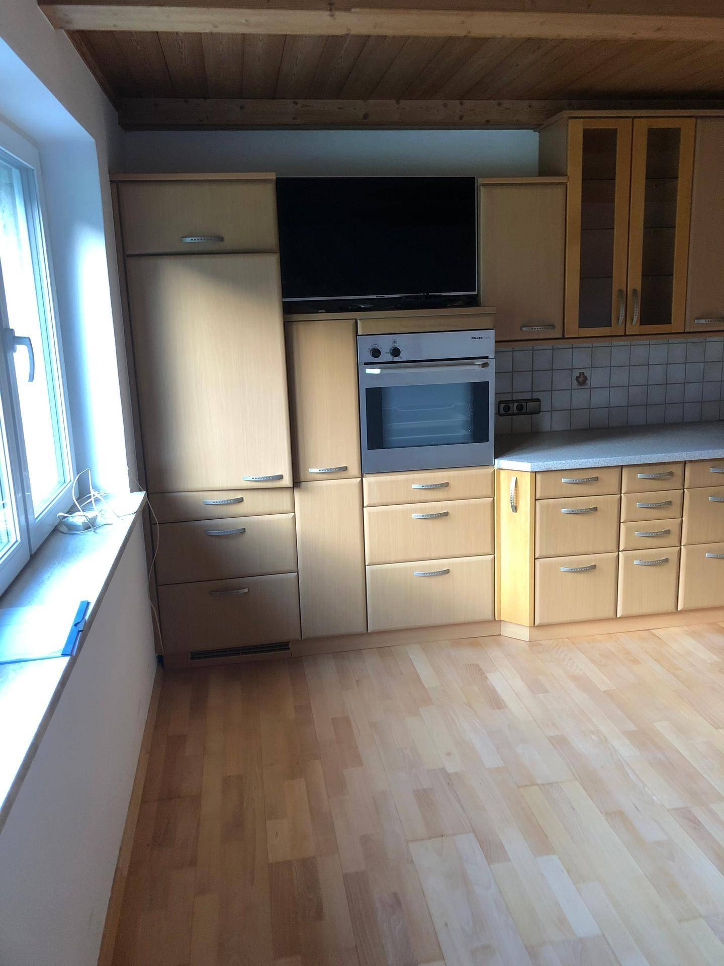 Küchenzeile mit integriertem Backofen, Kühlschrank und Oberschränken unter Holzbalkendecke.