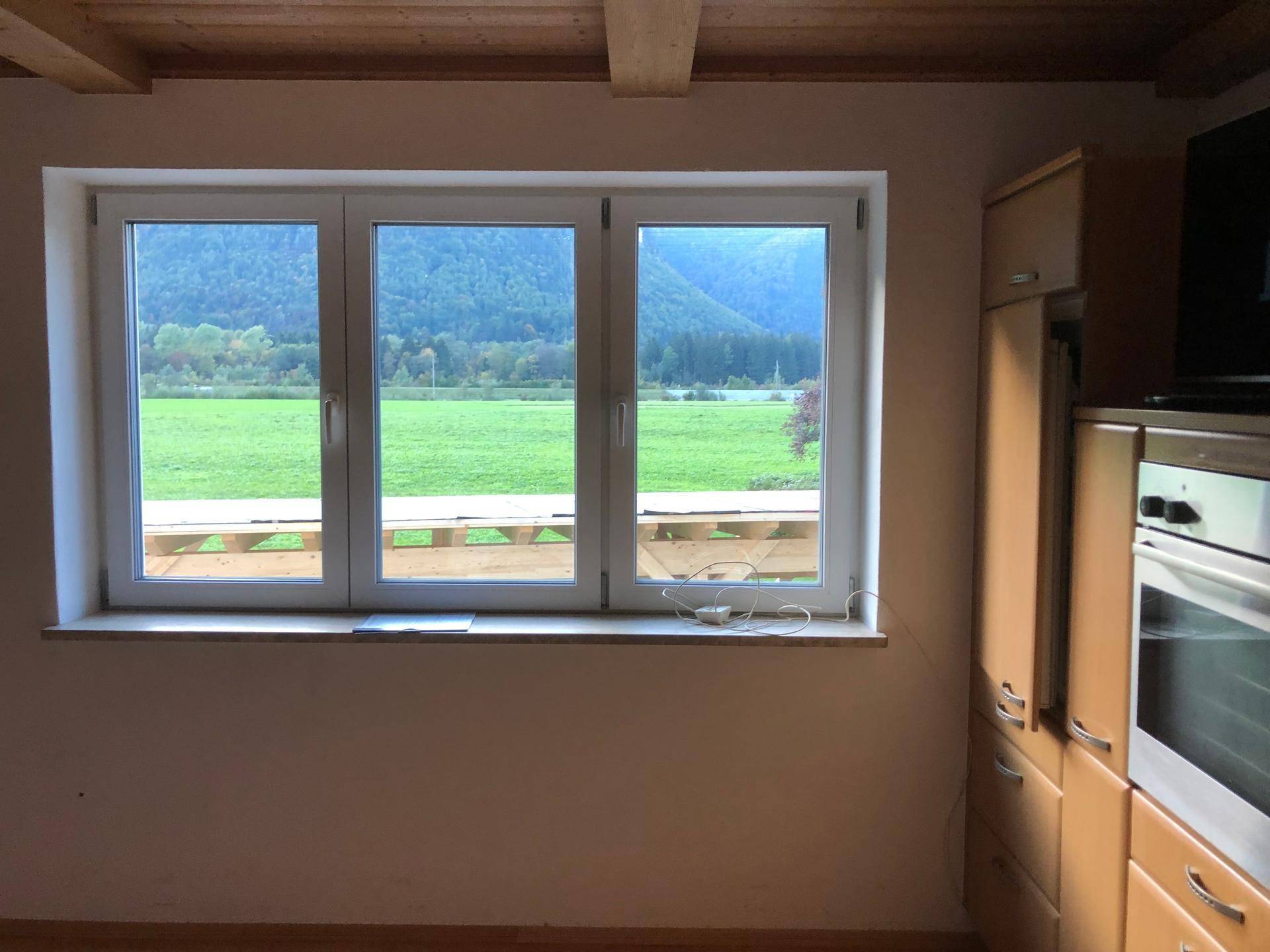 Helle Küche mit weitem Blick auf grüne Wiesen und Berge durch große Fenster.
