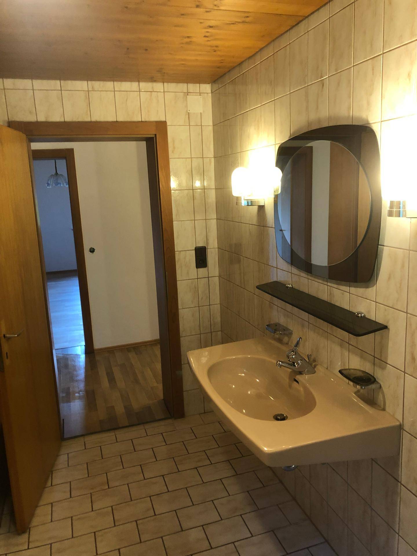 Badezimmer mit gefliesten Wänden, Holzdecke und einem Waschbecken im 80er-Jahre-Stil.