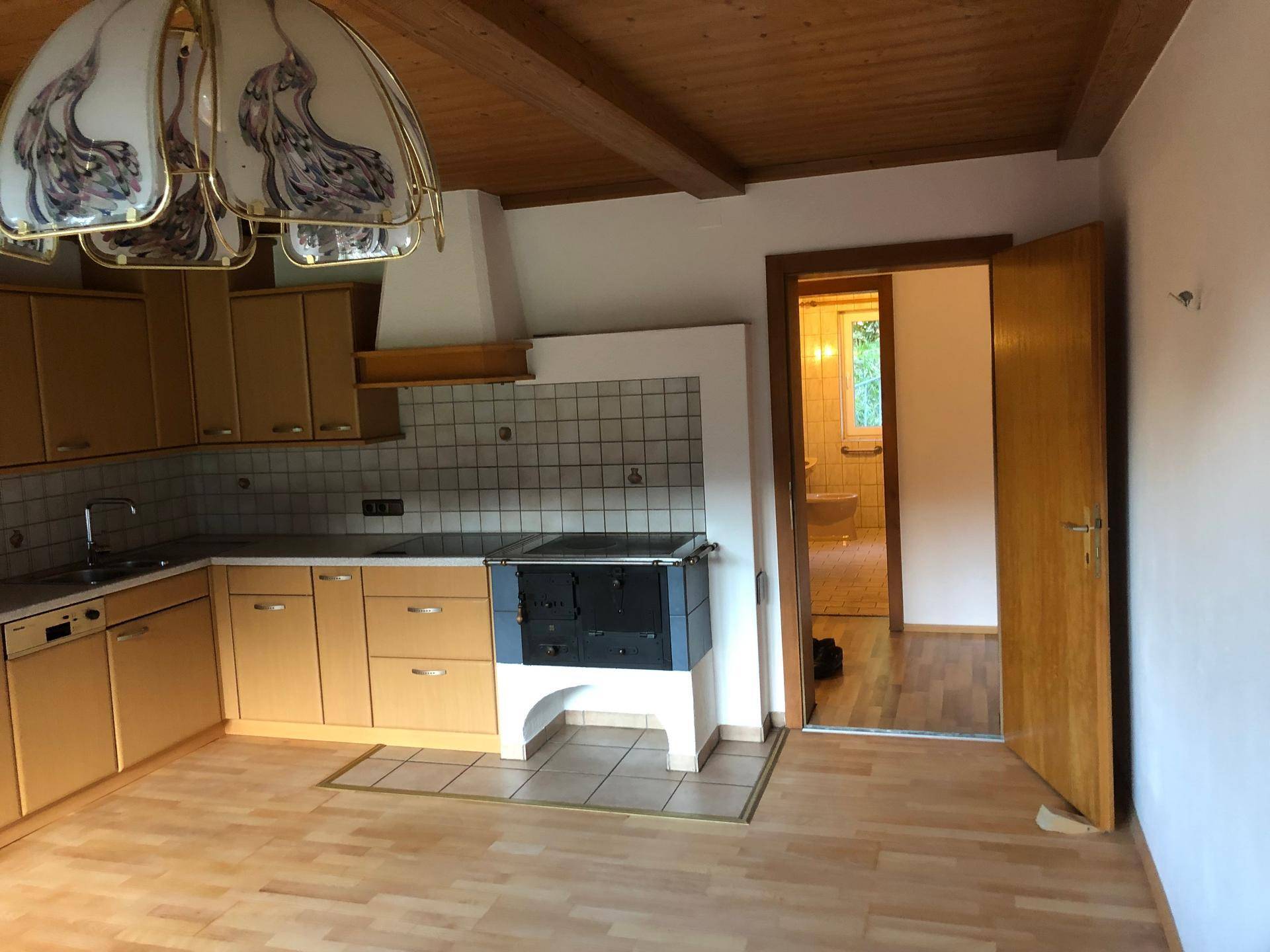 Küche mit traditionellem Holzherd, Einbauschränken und Zugang zu einem weiteren Raum.