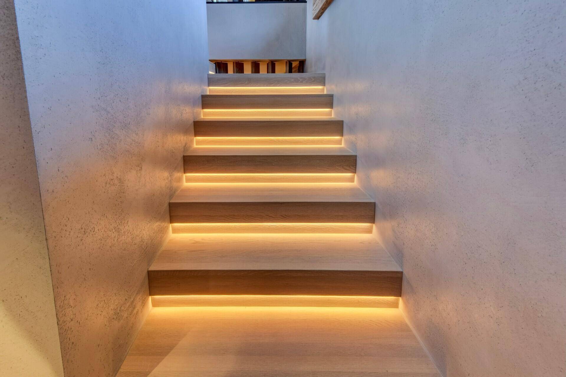 Moderne Treppe mit indirekter Beleuchtung, die eine warme und einladende Atmosphäre schafft.