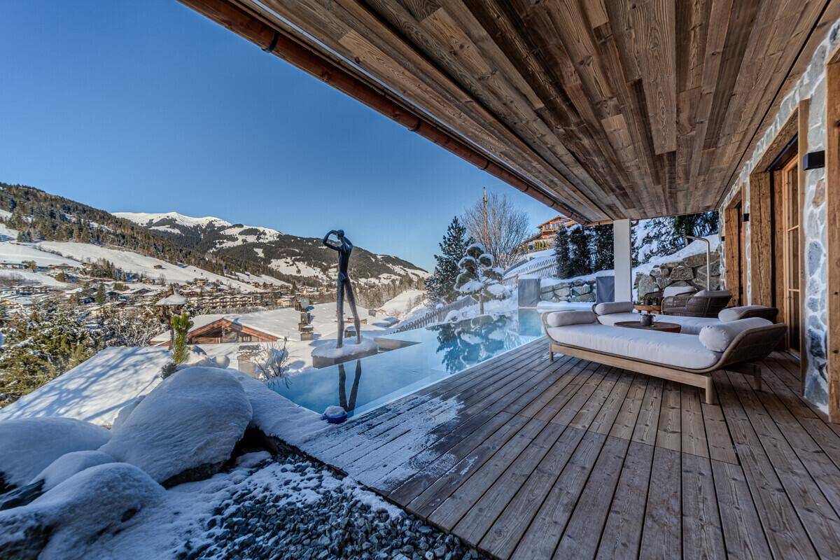 Luxuriöse Terrasse mit Infinity-Pool, Liegemöbeln und weitem Blick auf die verschneite Bergwelt.