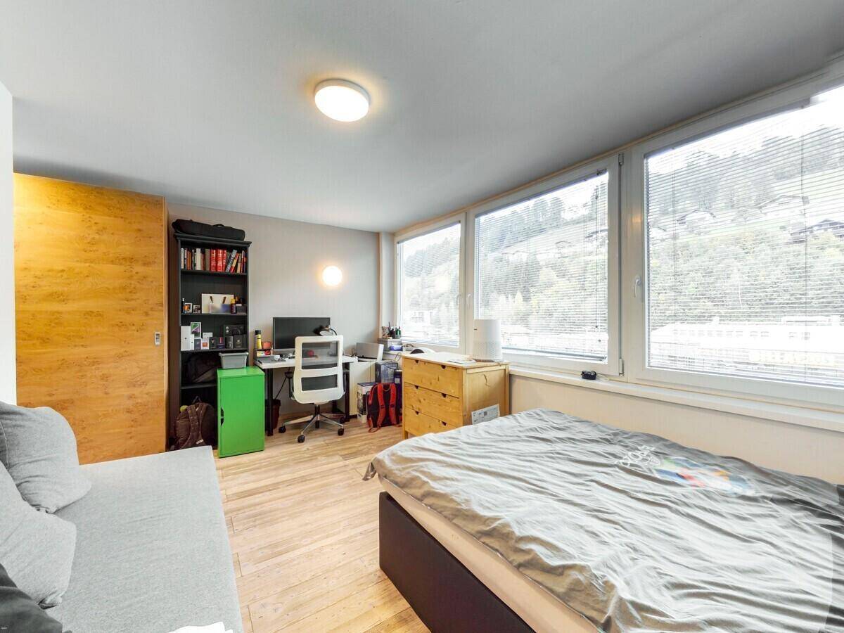 Helles Schlafzimmer mit Holzboden, Schreibtisch und großen Fenstern mit Bergblick.