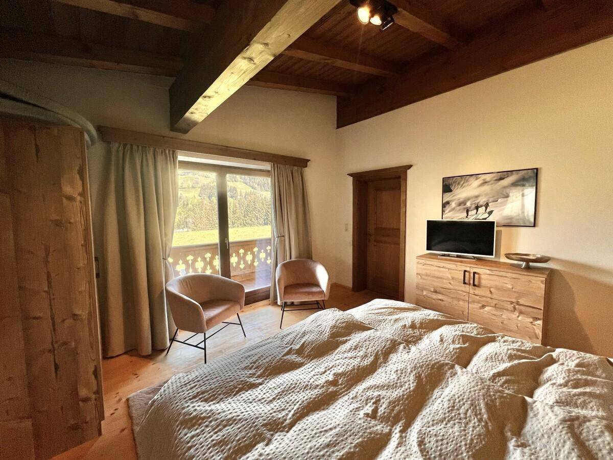 Helles Schlafzimmer mit Holzbalkendecke, TV und einem Balkon mit weitem Bergblick.
