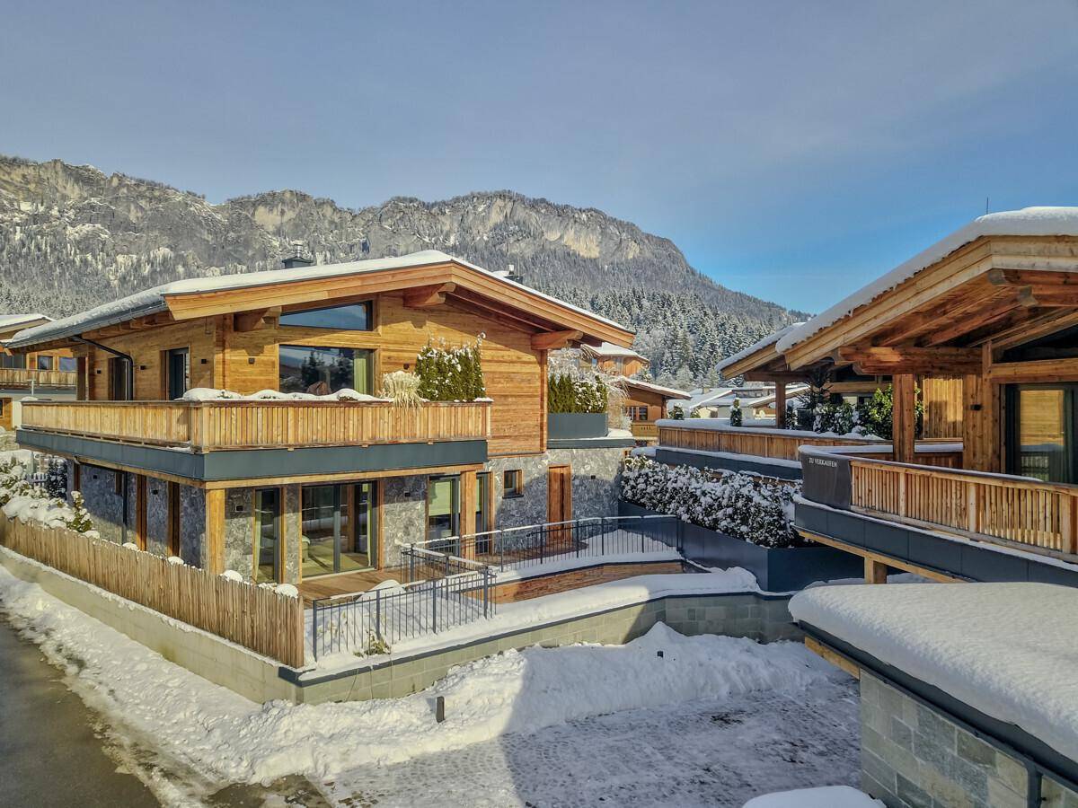 Moderne Chalets mit Holzfassaden und schneebedeckten Dächern in alpiner Umgebung.