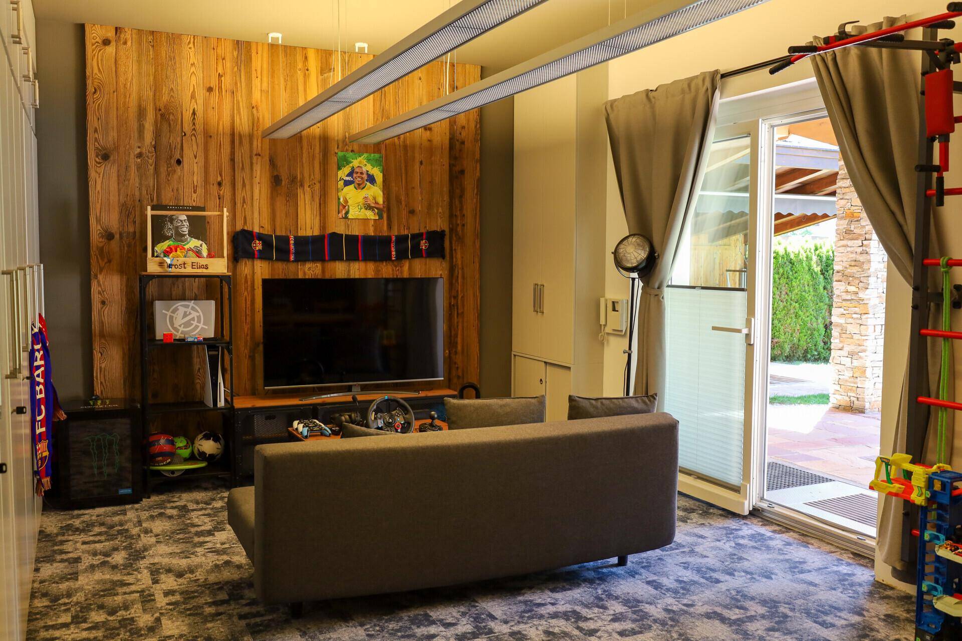 Modernes Wohnzimmer mit Holzwand, großem Fernseher und Zugang zum Außenbereich.